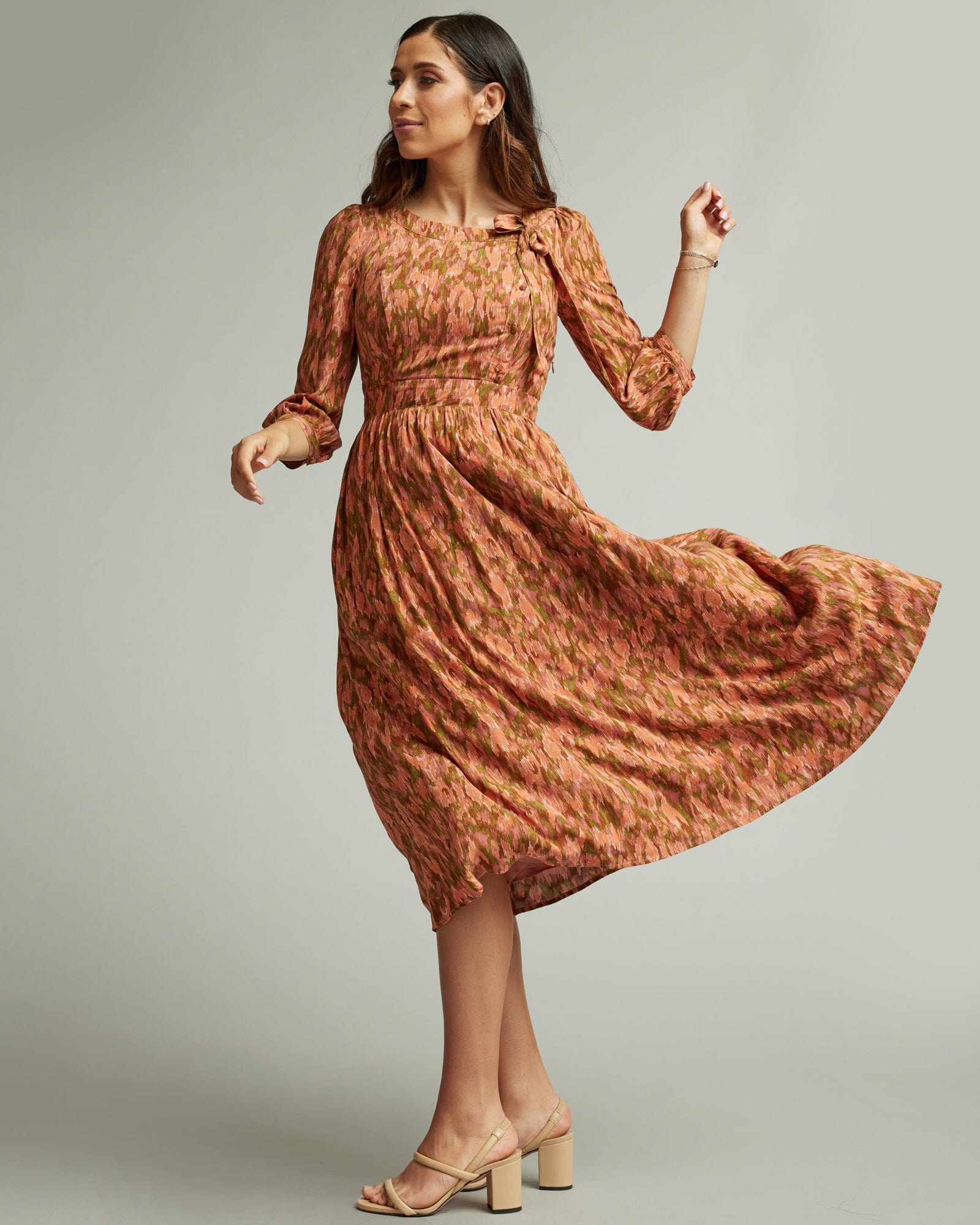 Woman in a 3/4 length sleeve, midi-length dress in orange and brown.