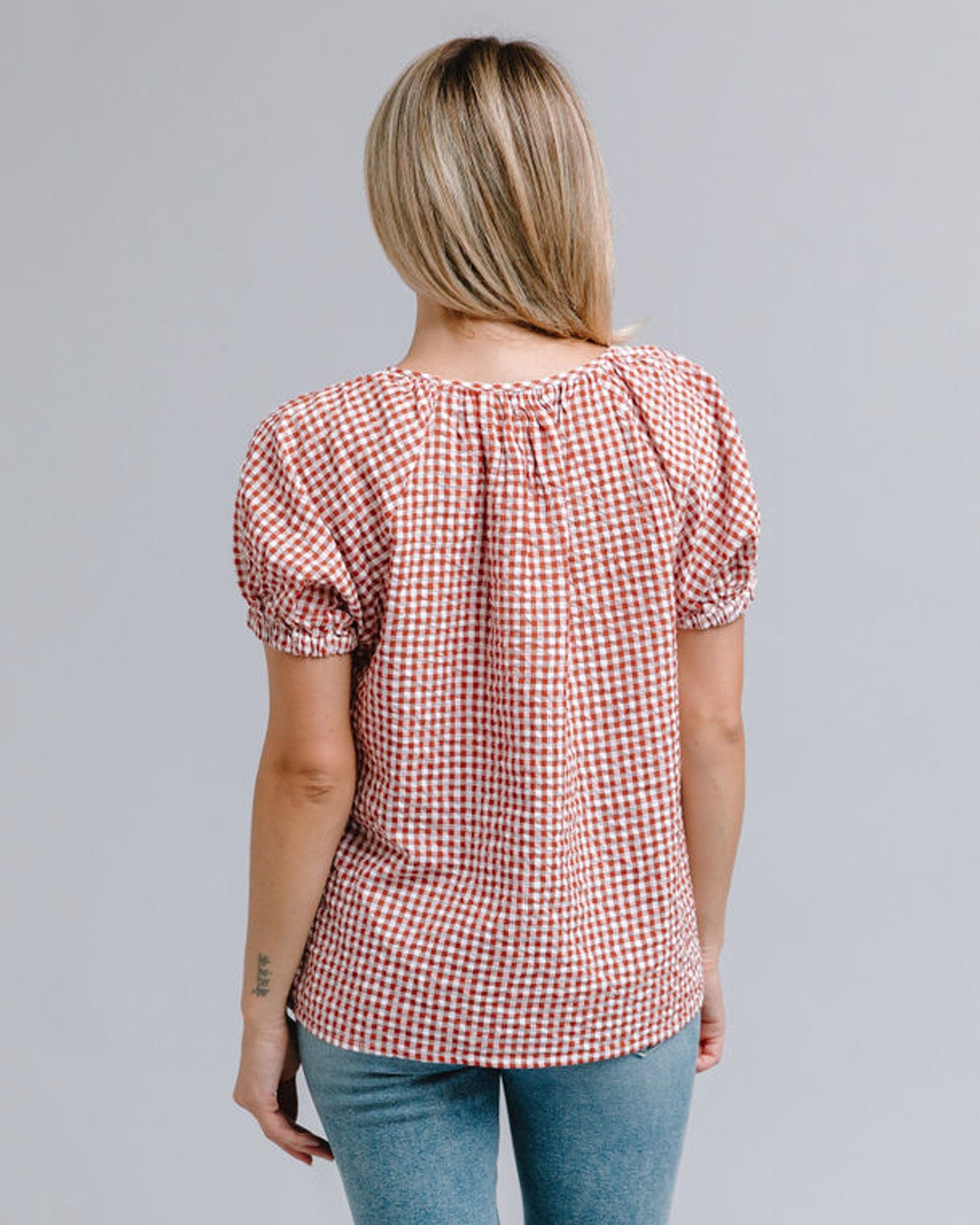 Woman in a red and white plaid, short sleeve, v-neck top with lace along neckline