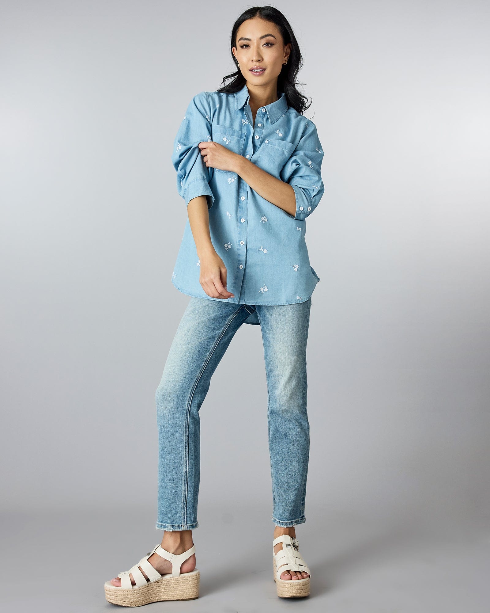 Woman in a long sleeve, chambray button-down top with floral embroidery.