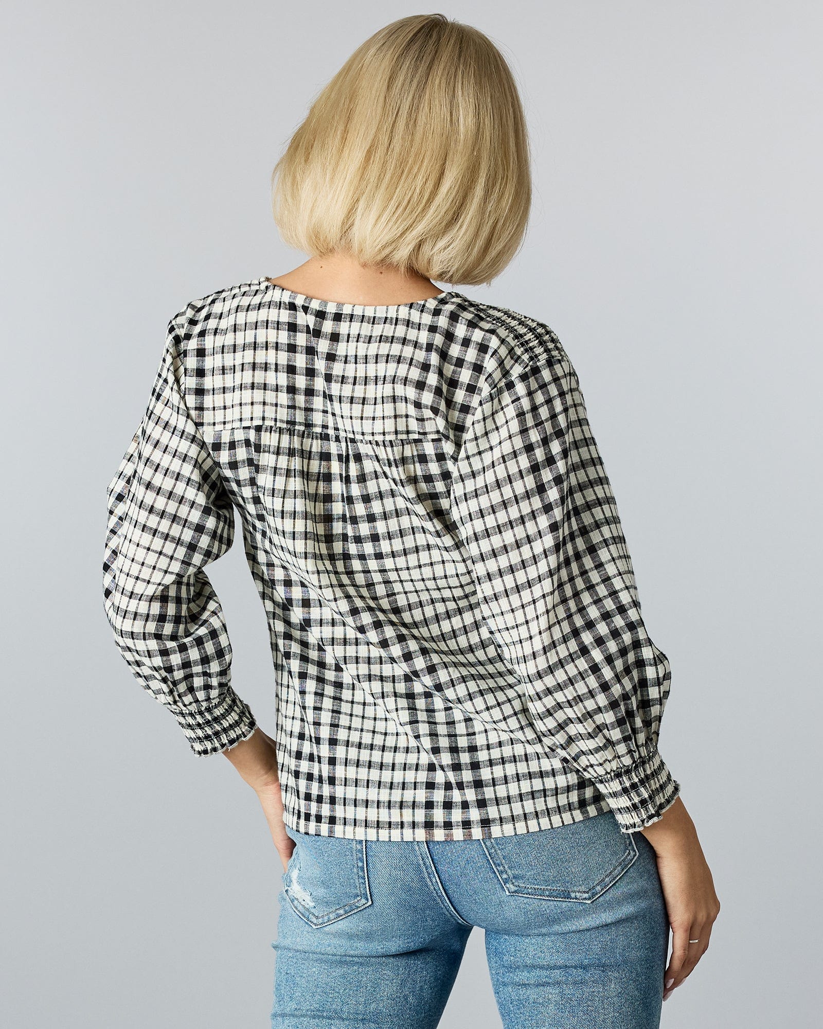 Woman in a 3/4 length v-neck blouse with plaid pattern and buttons down front.