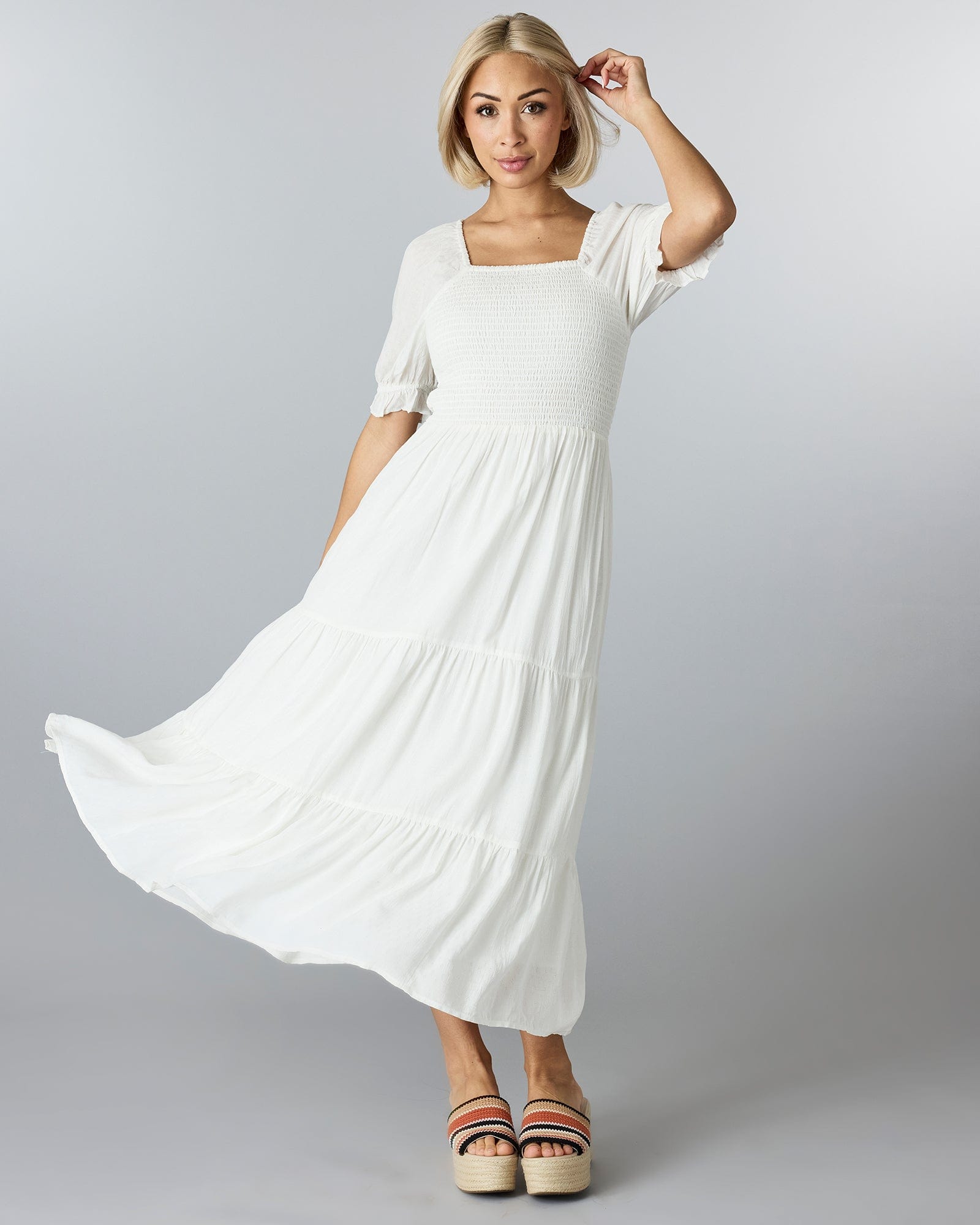 Woman in a white, half sleeved dress with a square neckline and tiers down the skirt.