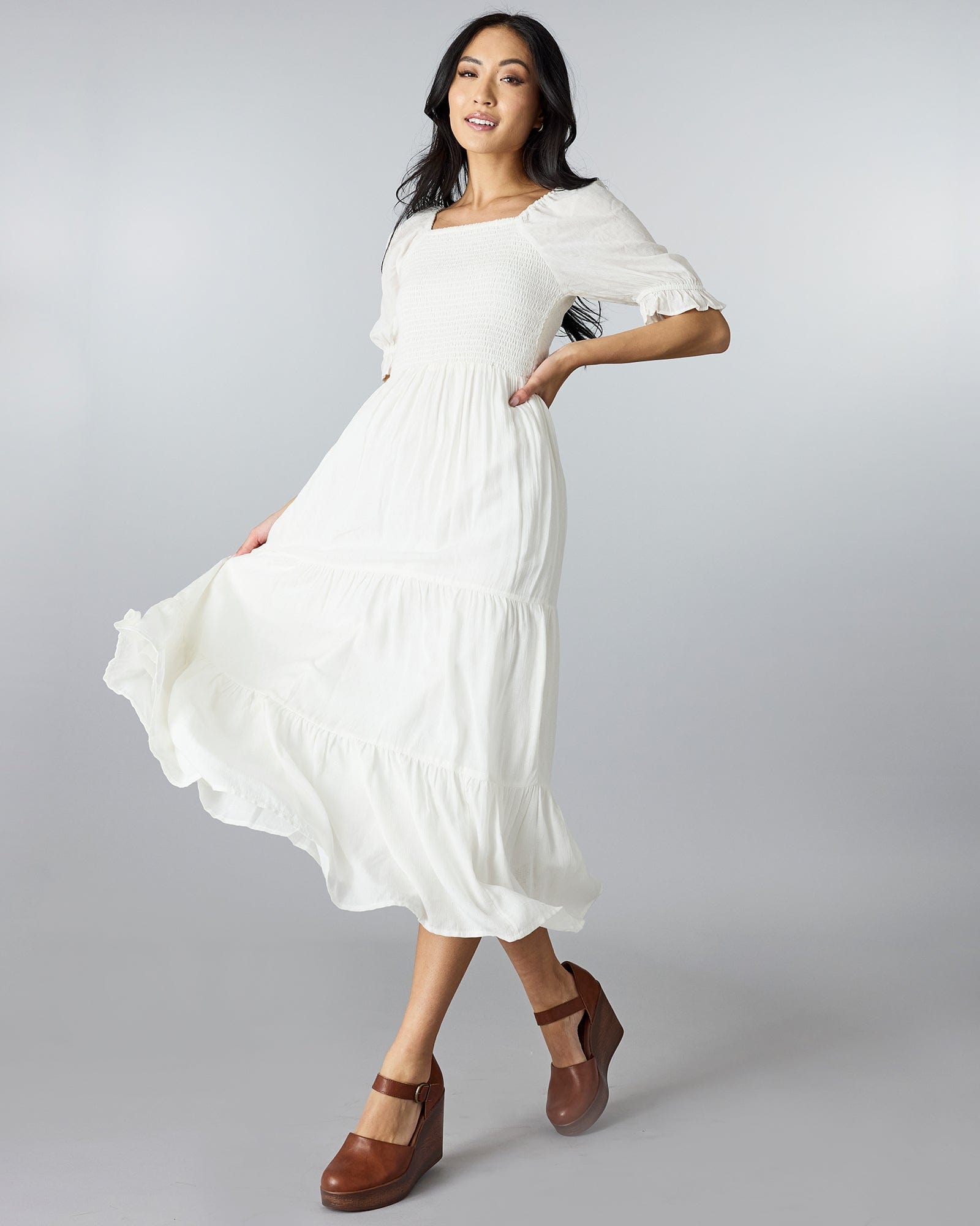 Woman in a white, half sleeved dress with a square neckline and tiers down the skirt.