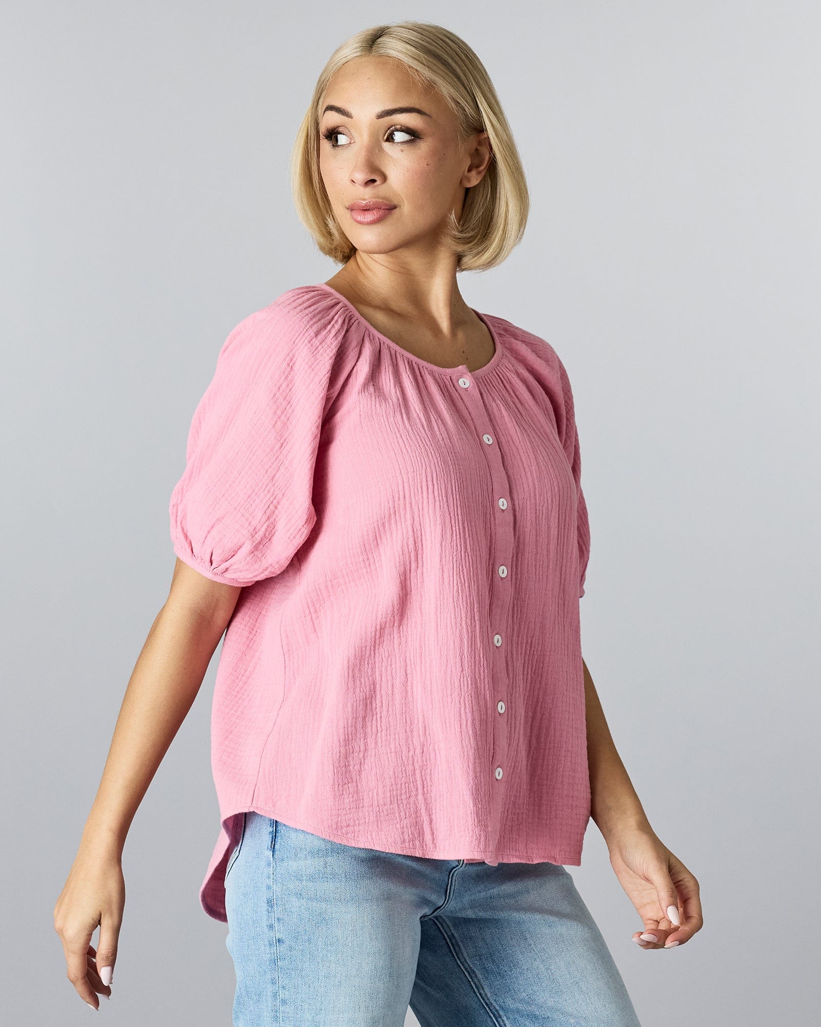 Woman in a short sleeved, pink blouse with buttons down the front and slight texturing of material