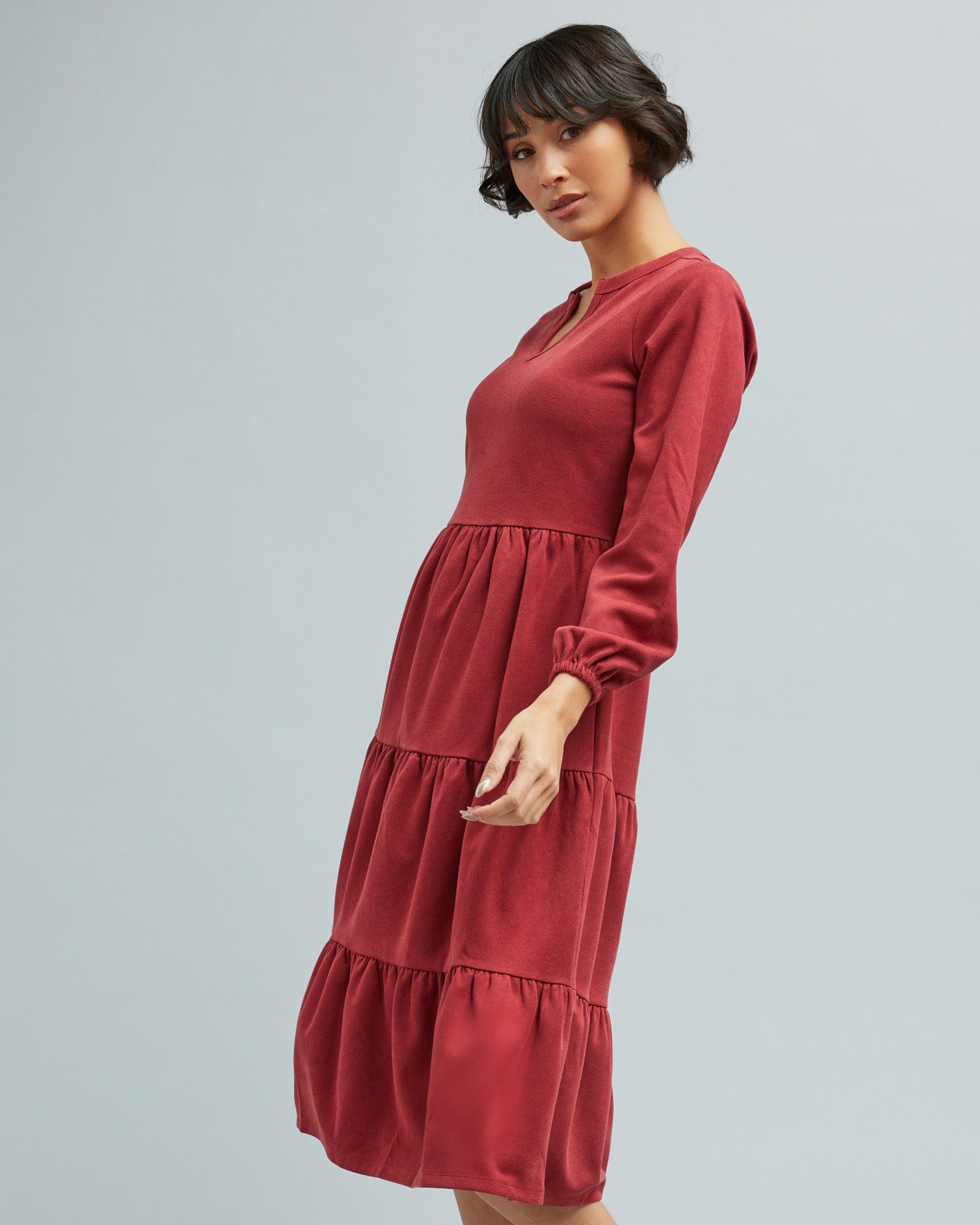 Woman in a long sleeve, tiered skirt, brick red dress.
