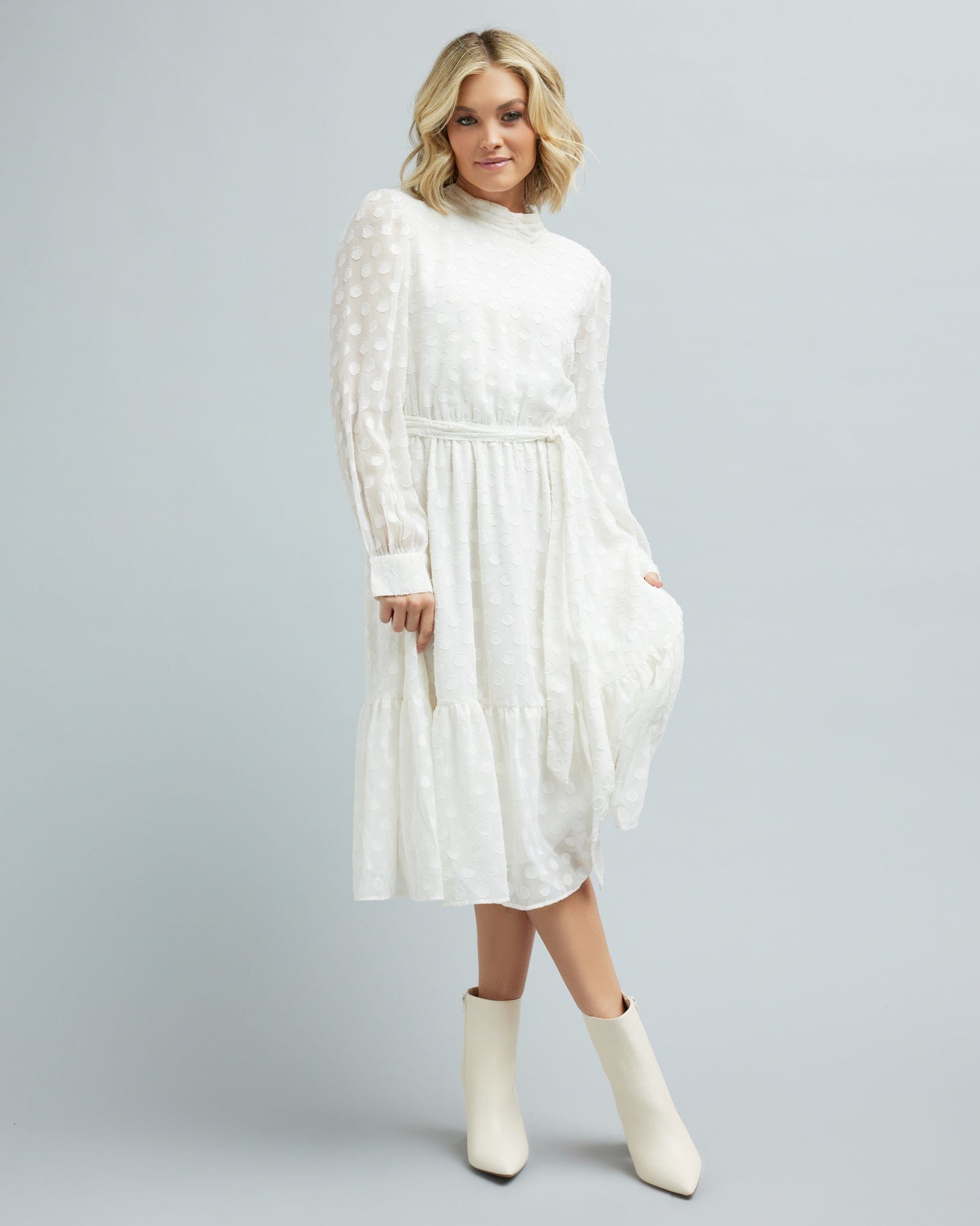 Woman in a long sleeve, white, midi length dress with white polka dots