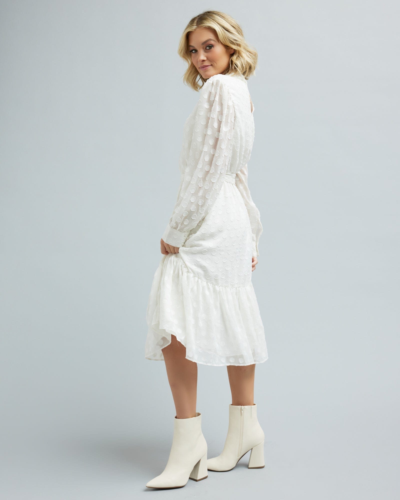Woman in a long sleeve, white, midi length dress with white polka dots