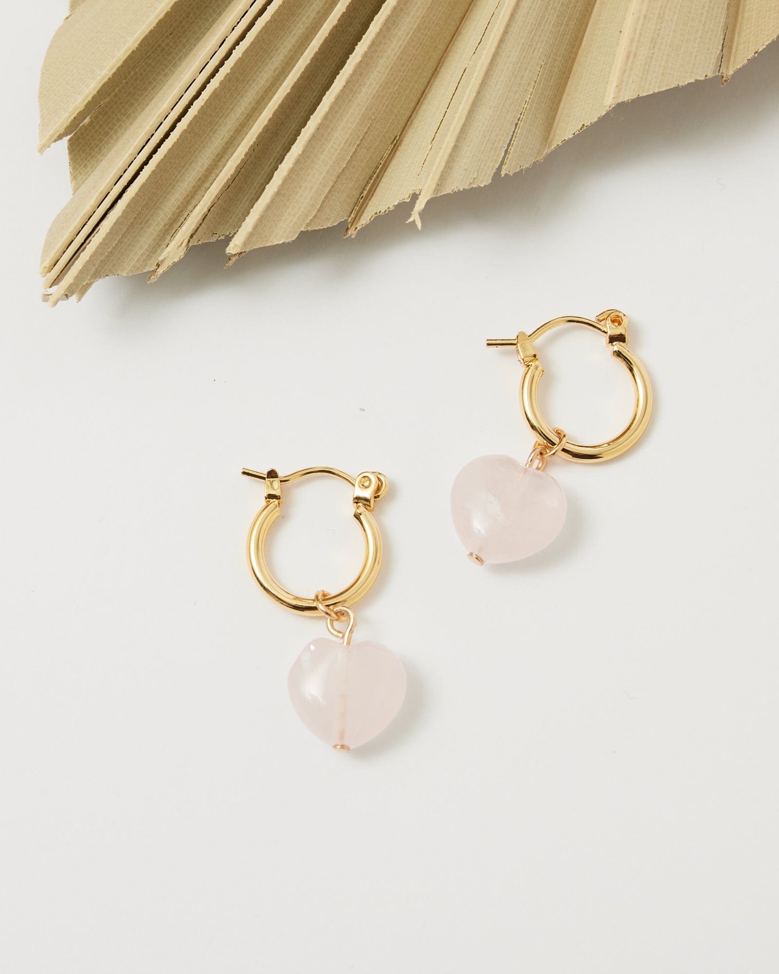 Gold huggie hoop earrings with heart shaped rose quartz bead on end.