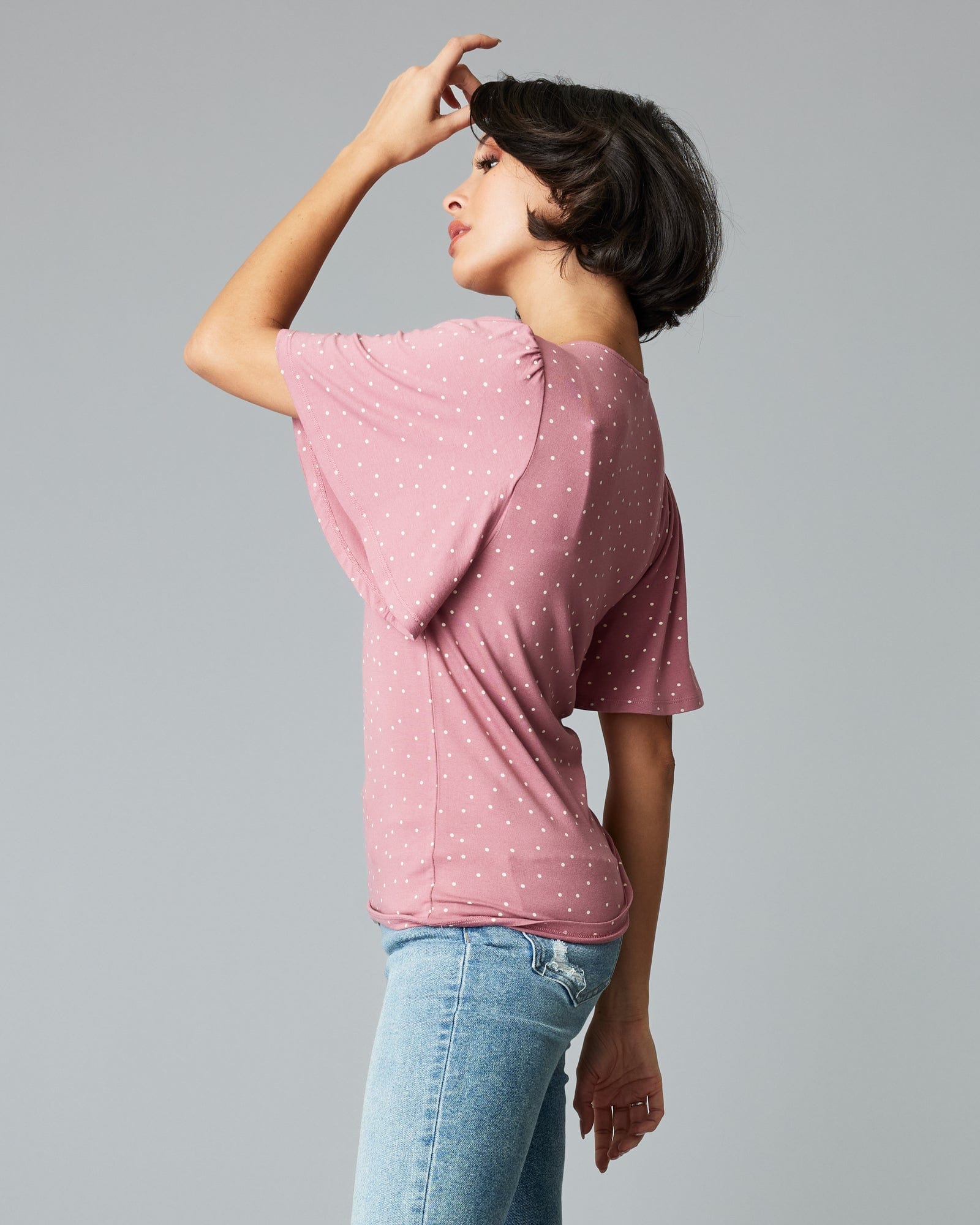 Woman in a short flutter sleee, v-neck, pink with white polka dots top.