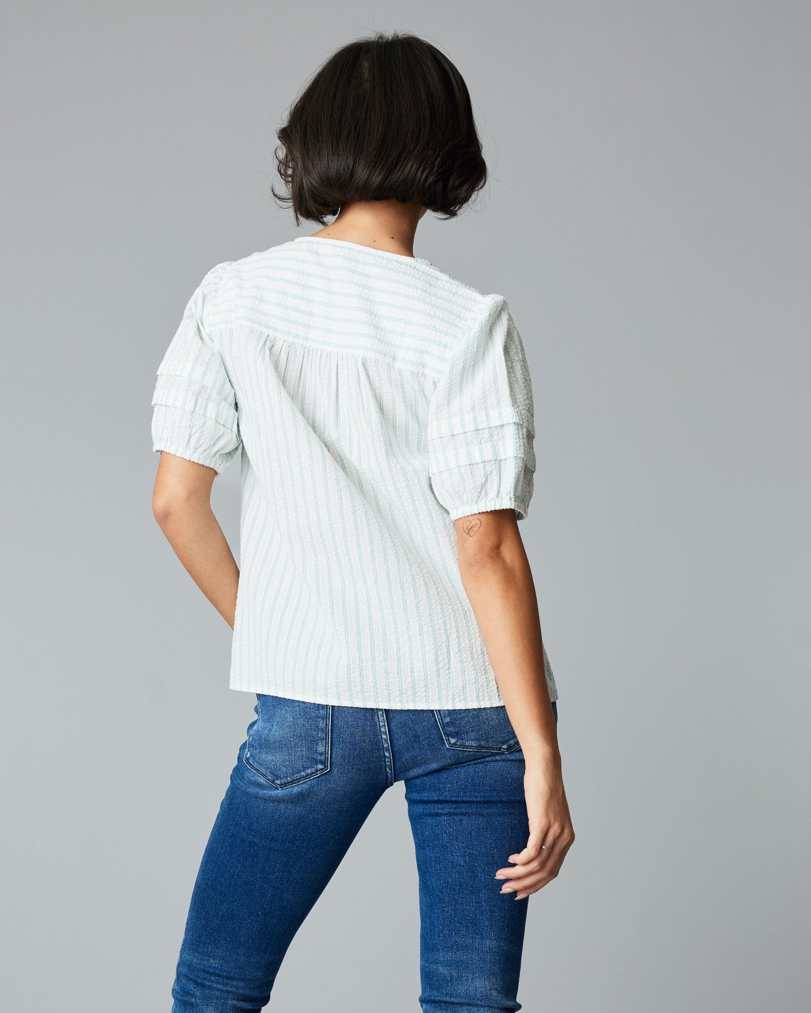 Woman in a short sleeve, v-neck, white and green vertical striped blouse.