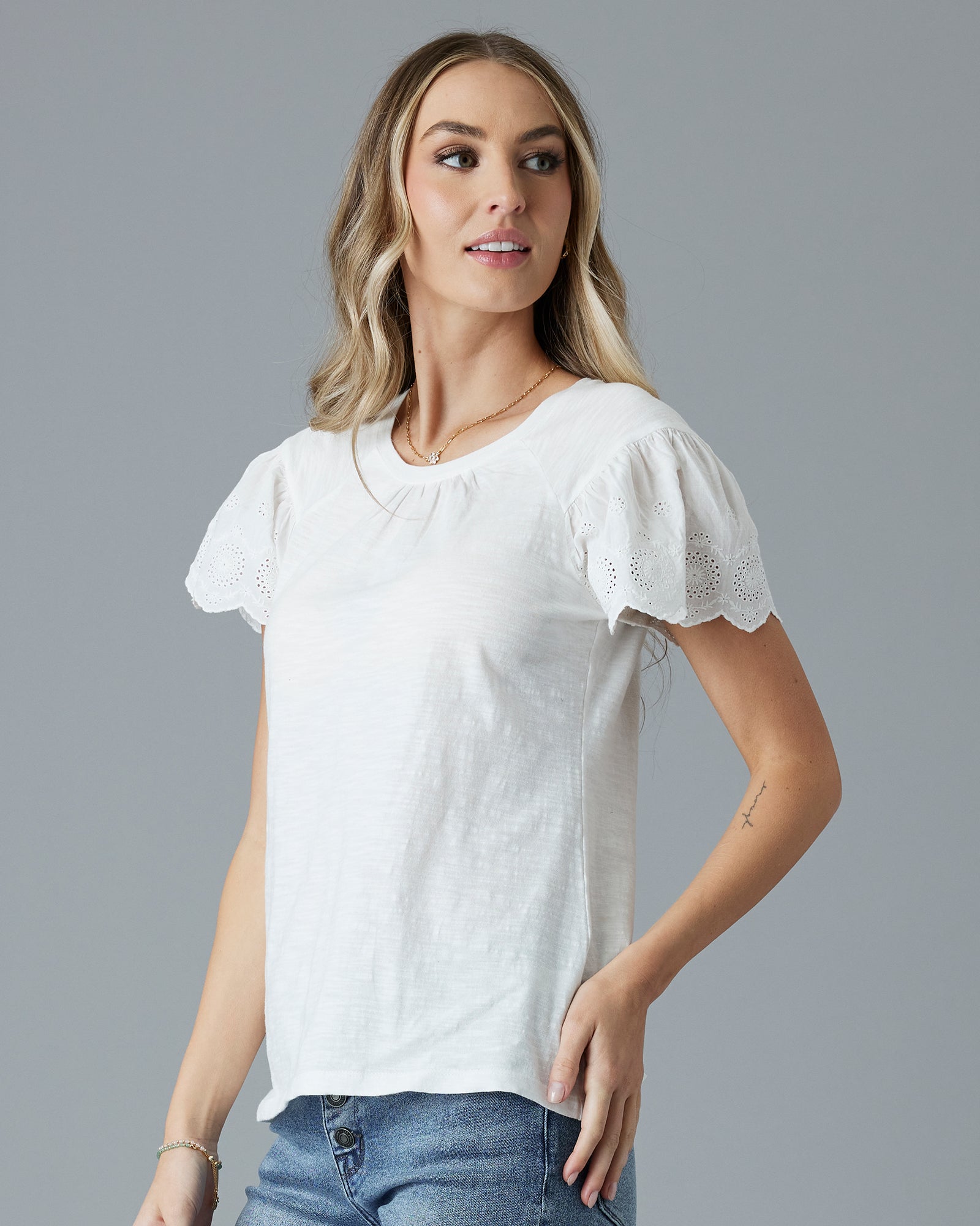 Woman in a white, short sleeved t-shirt with eyelet detail on sleeves.