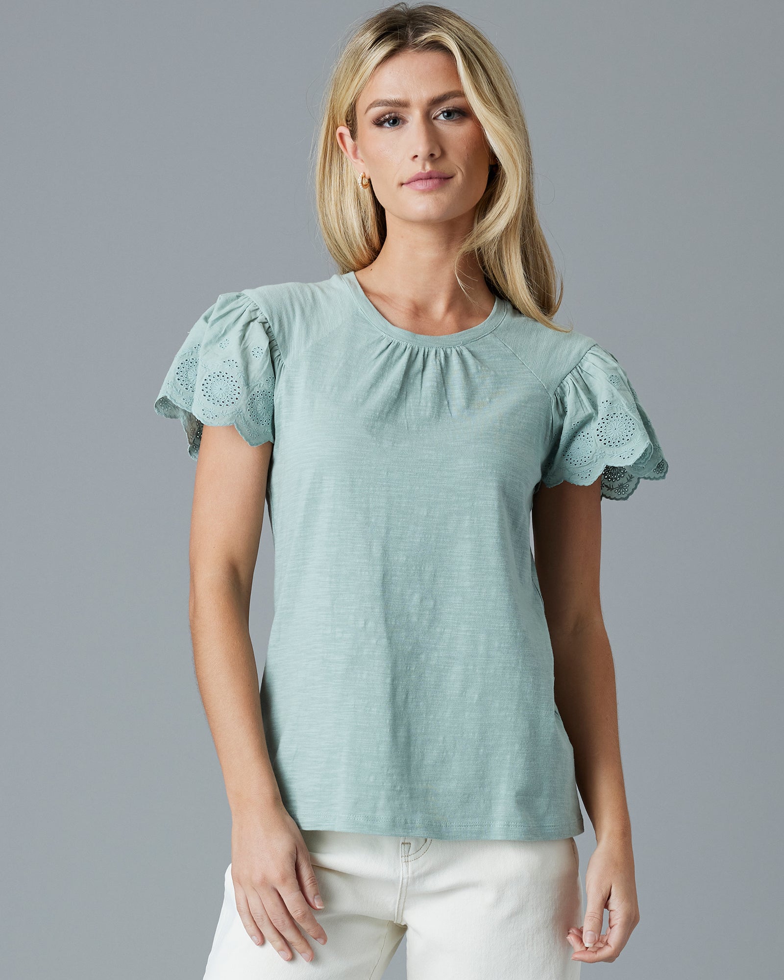 Woman in a green, short sleeved t-shirt with eyelet detail on sleeves.