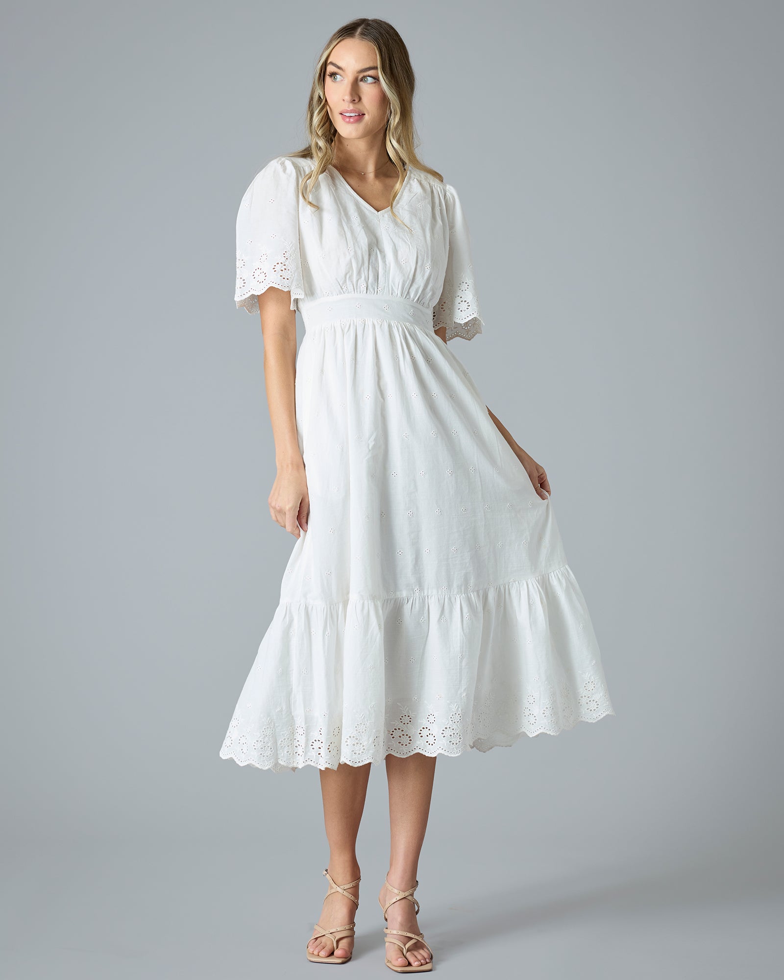 Woman in a white short sleeve, midi-length dress with eyelet details on hem