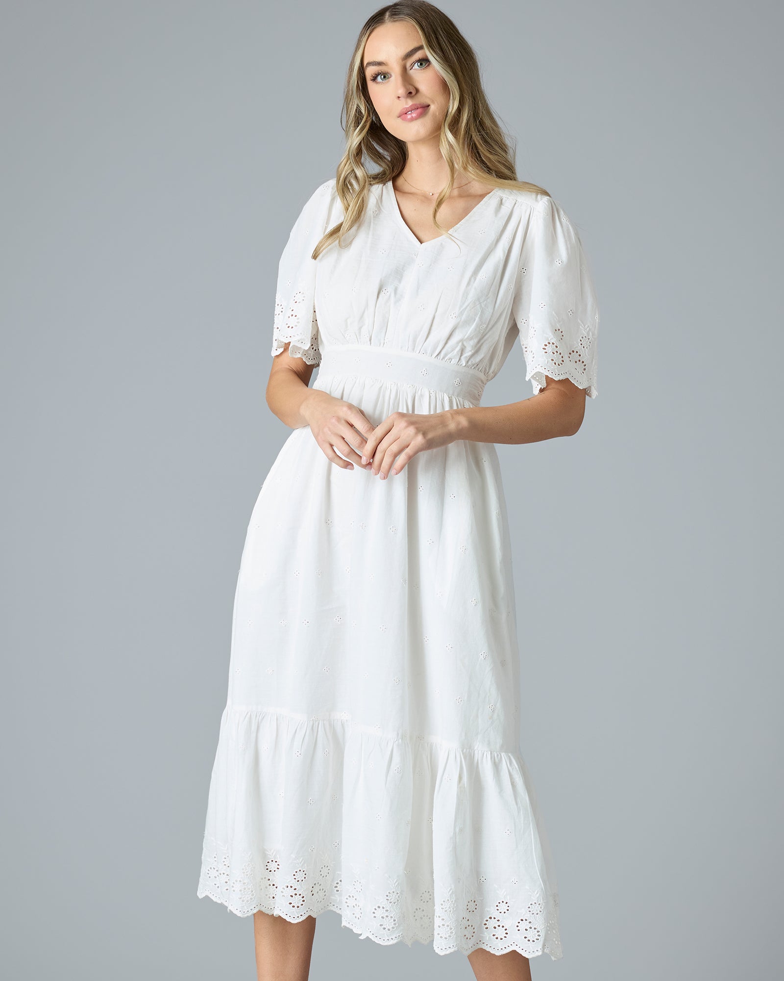 Woman in a white short sleeve, midi-length dress with eyelet details on hem