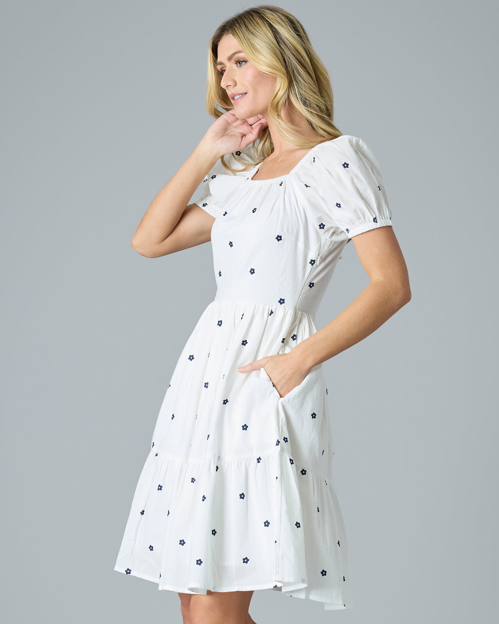 Woman in a white with blue flower dress that is knee-length and short sleeves