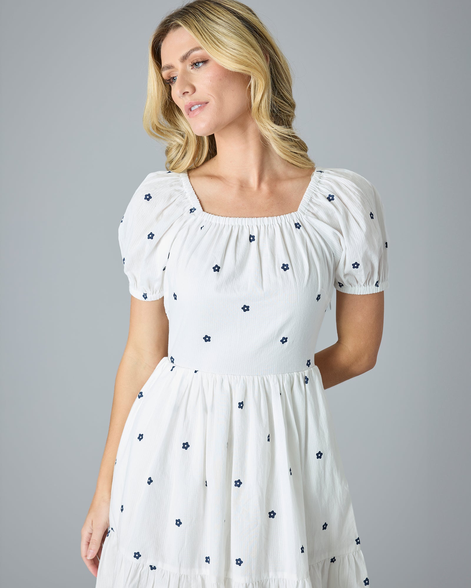 Woman in a white with blue flower dress that is knee-length and short sleeves