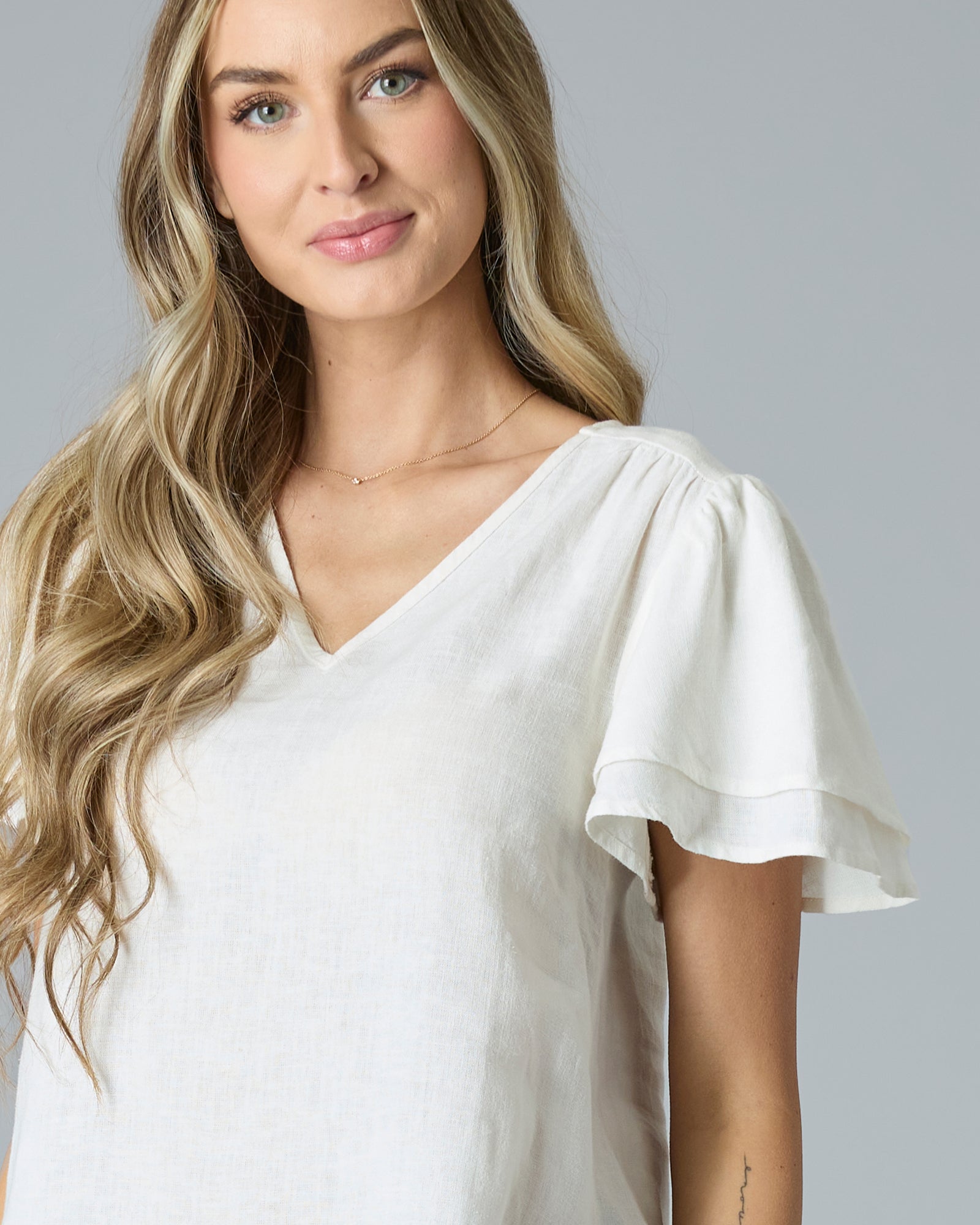 Close up of woman in cream colored short sleeve, v-neck linen blouse