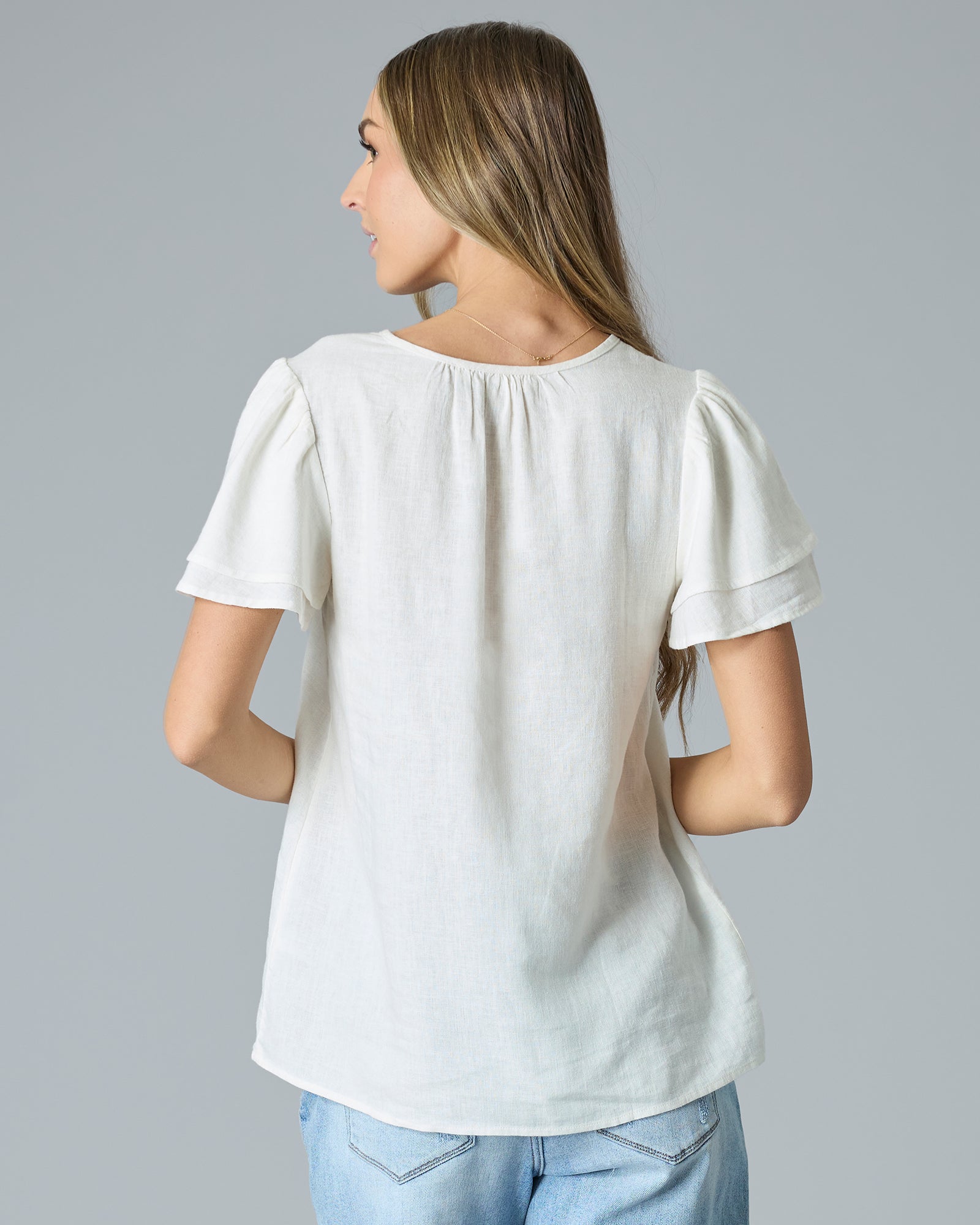 Back view of woman in cream colored short sleeve, v-neck linen blouse