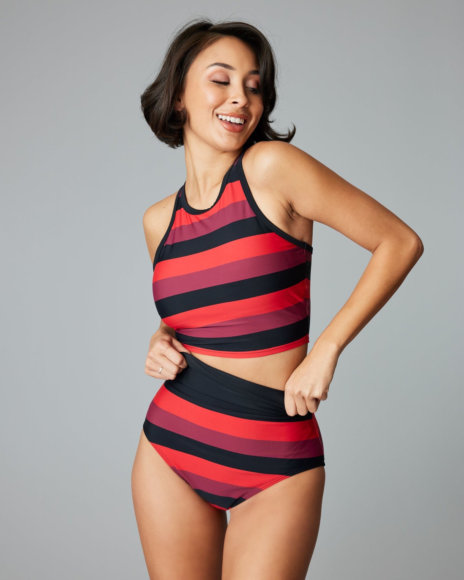 Woman in a two-piece swimsuit with red, plum and black striped bottoms.