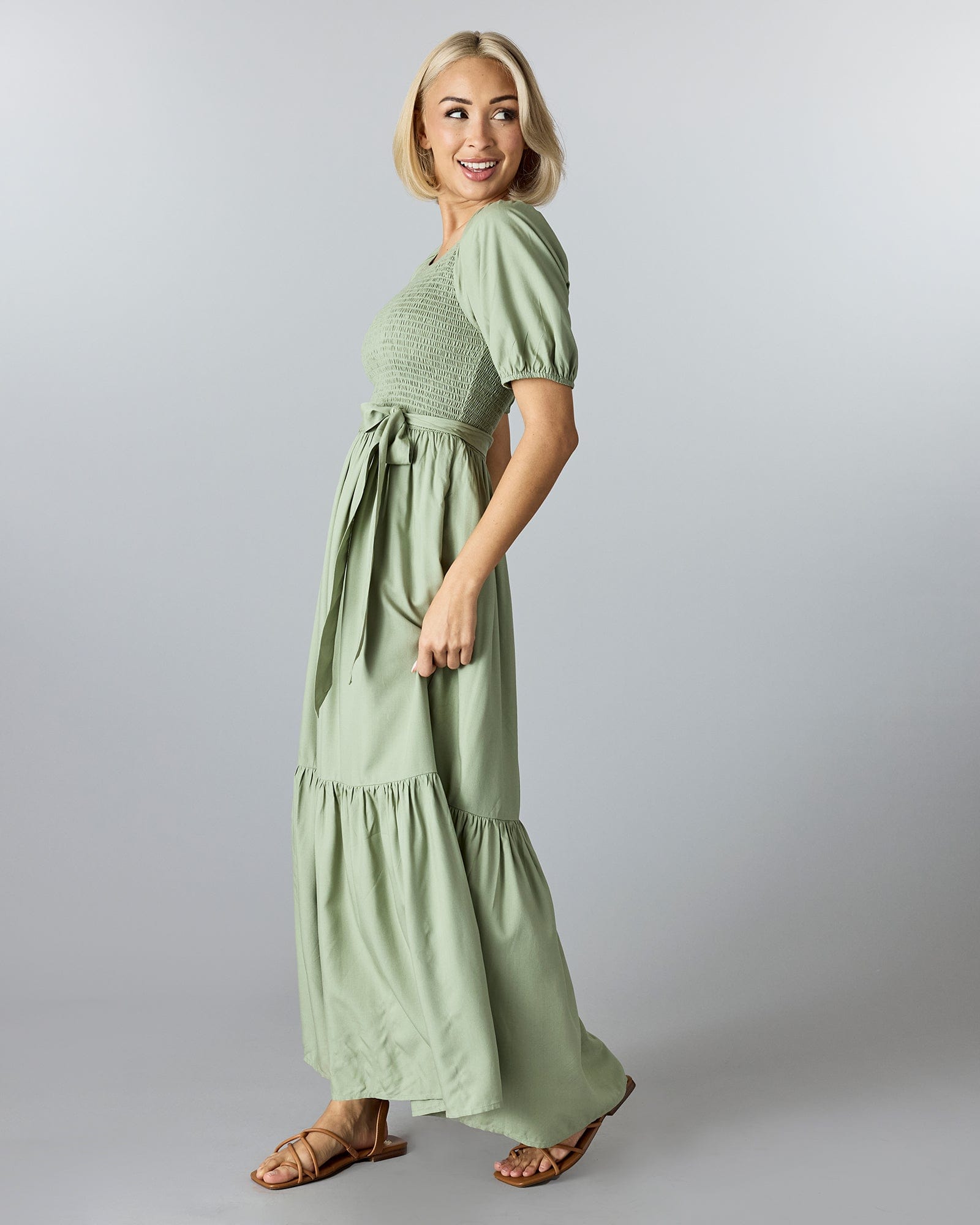 Woman in a green, short sleeved, maxi-length dress with smocking on bodice and a tie at the waist.
