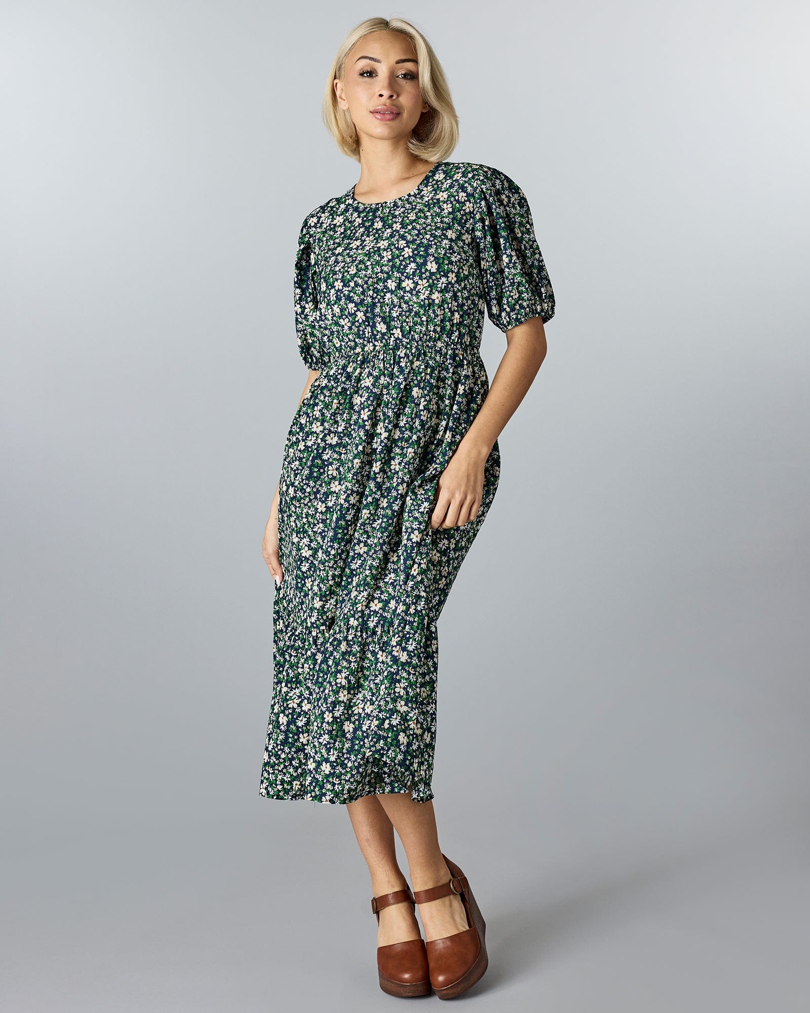 Woman in a blue and green floral, short sleeved, midi-length dress.