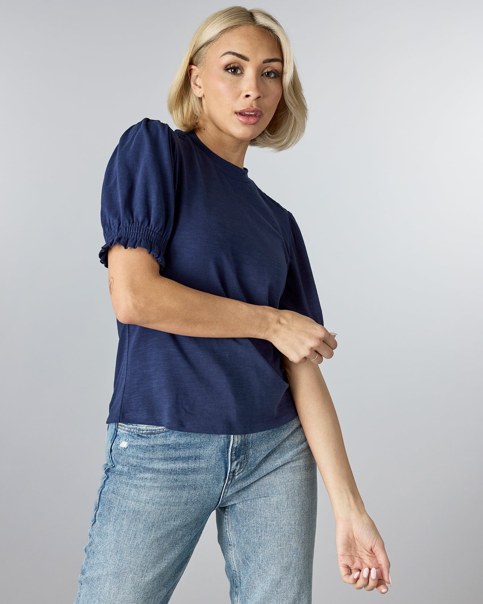 Woman in a blue short sleeved top that has puffed sleeves and a high neckline.
