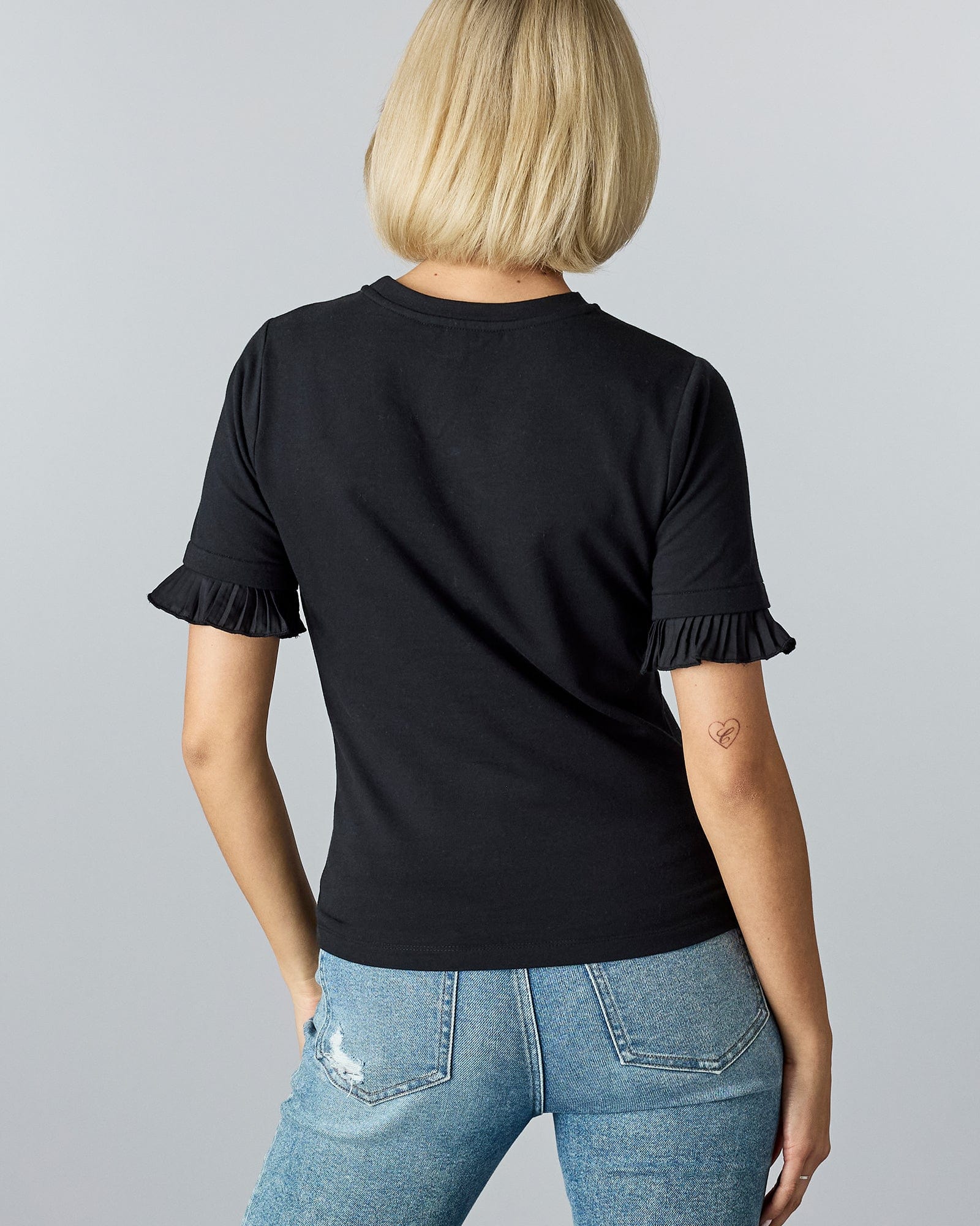 Woman in a black short sleeved top with ruffles on bottom of sleeve hem.