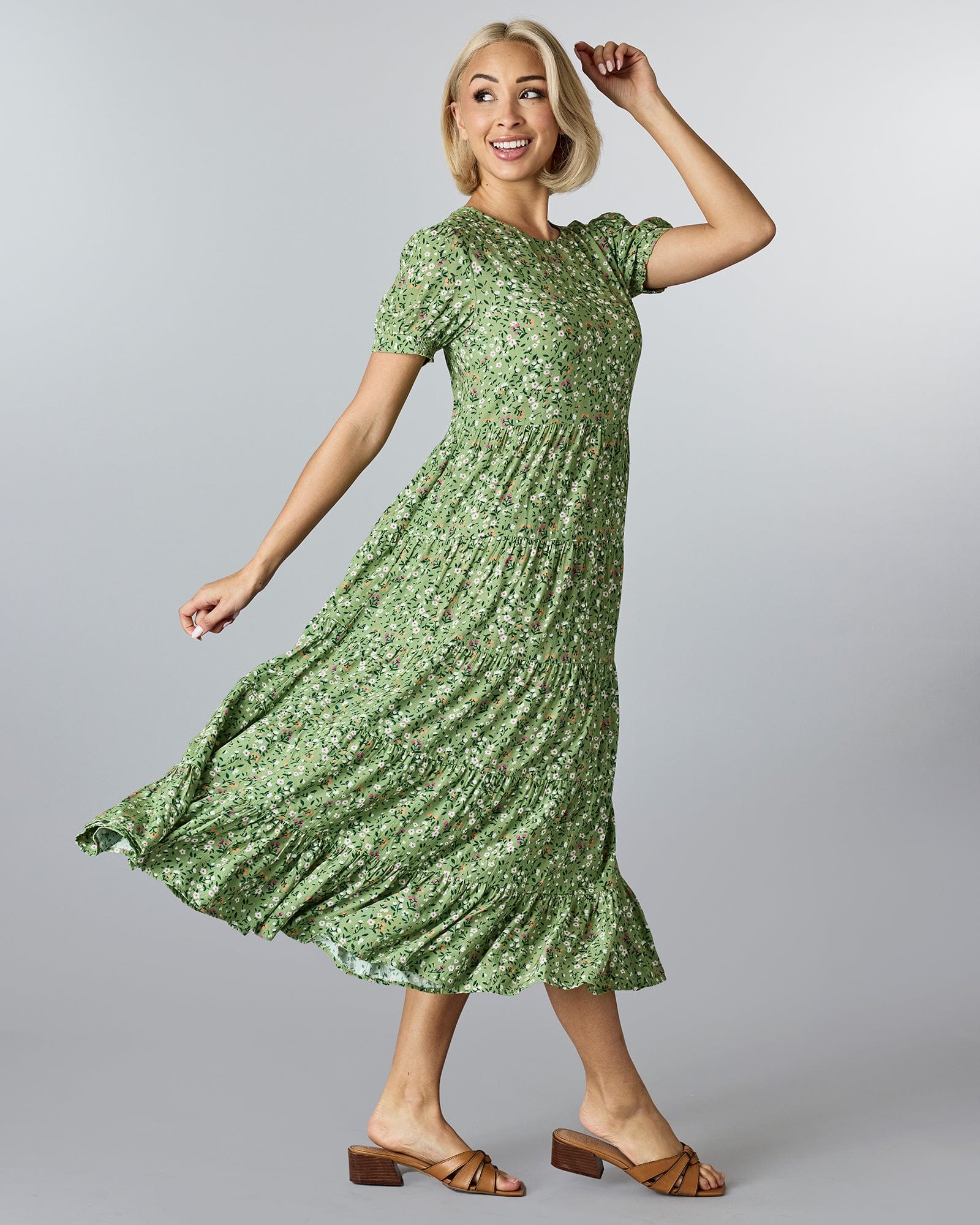 Woman in a green floral dress that has short sleeves and tiers down the skirt.