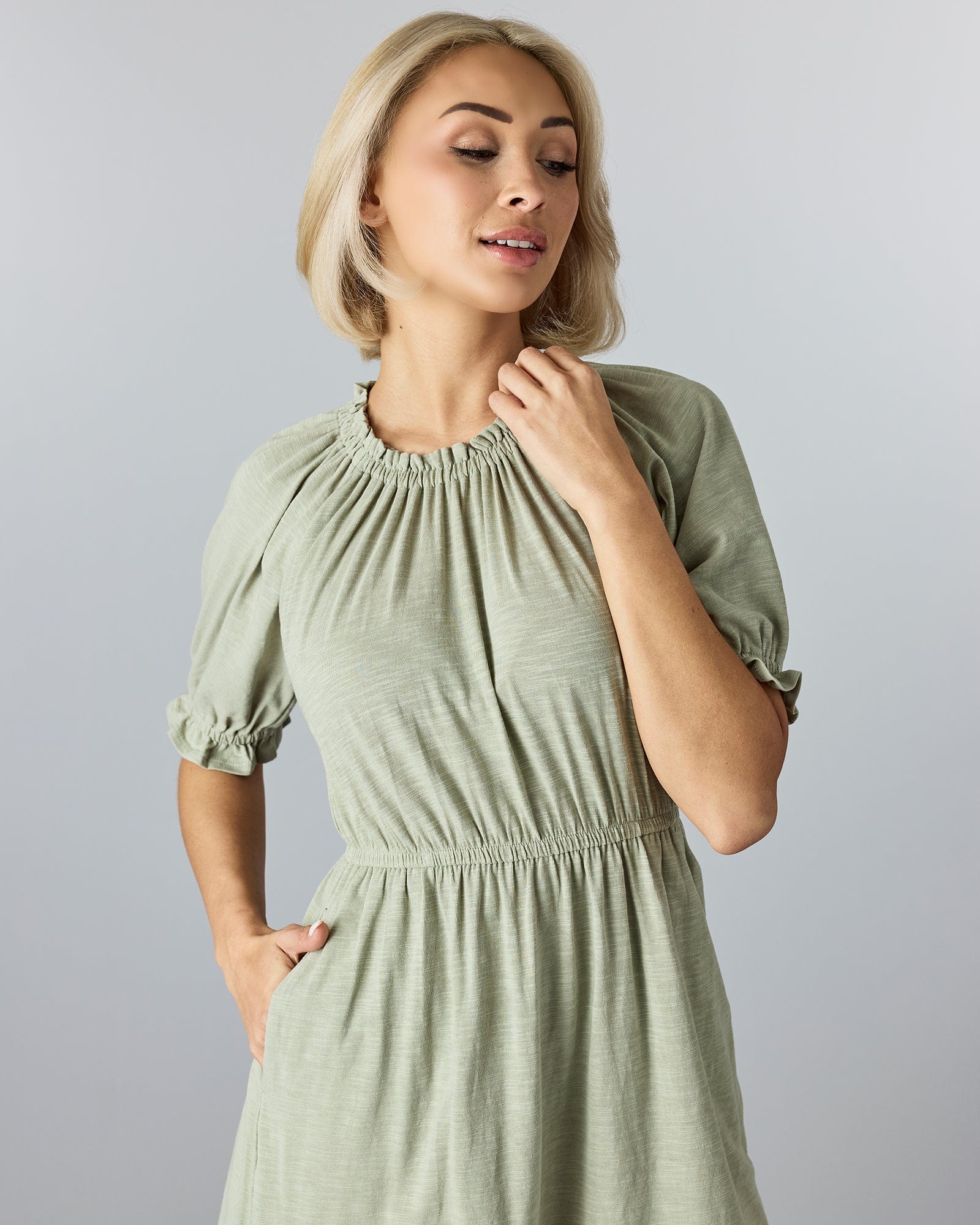 Woman in a green, knee-length, short sleeve dress with a high neckline and ruffles at neck and arms.