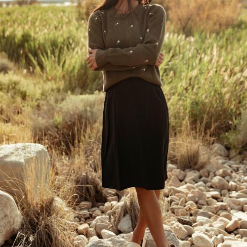 A women in a dark olive sweater and a black skirt. Shop bottoms