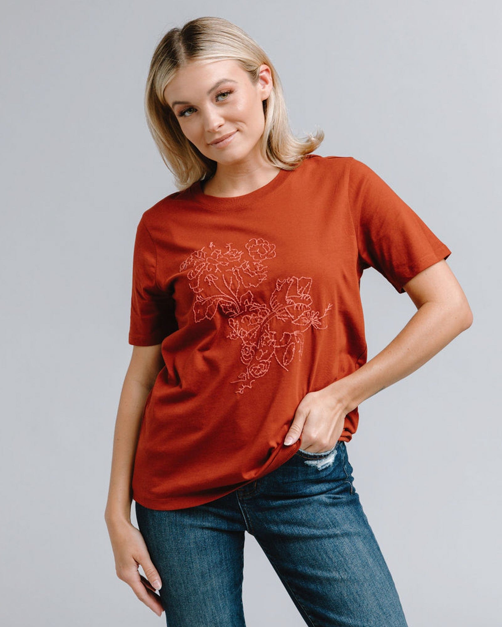 Woman in a short sleeve, burnt orange, graphic tee with embroidered floral on front