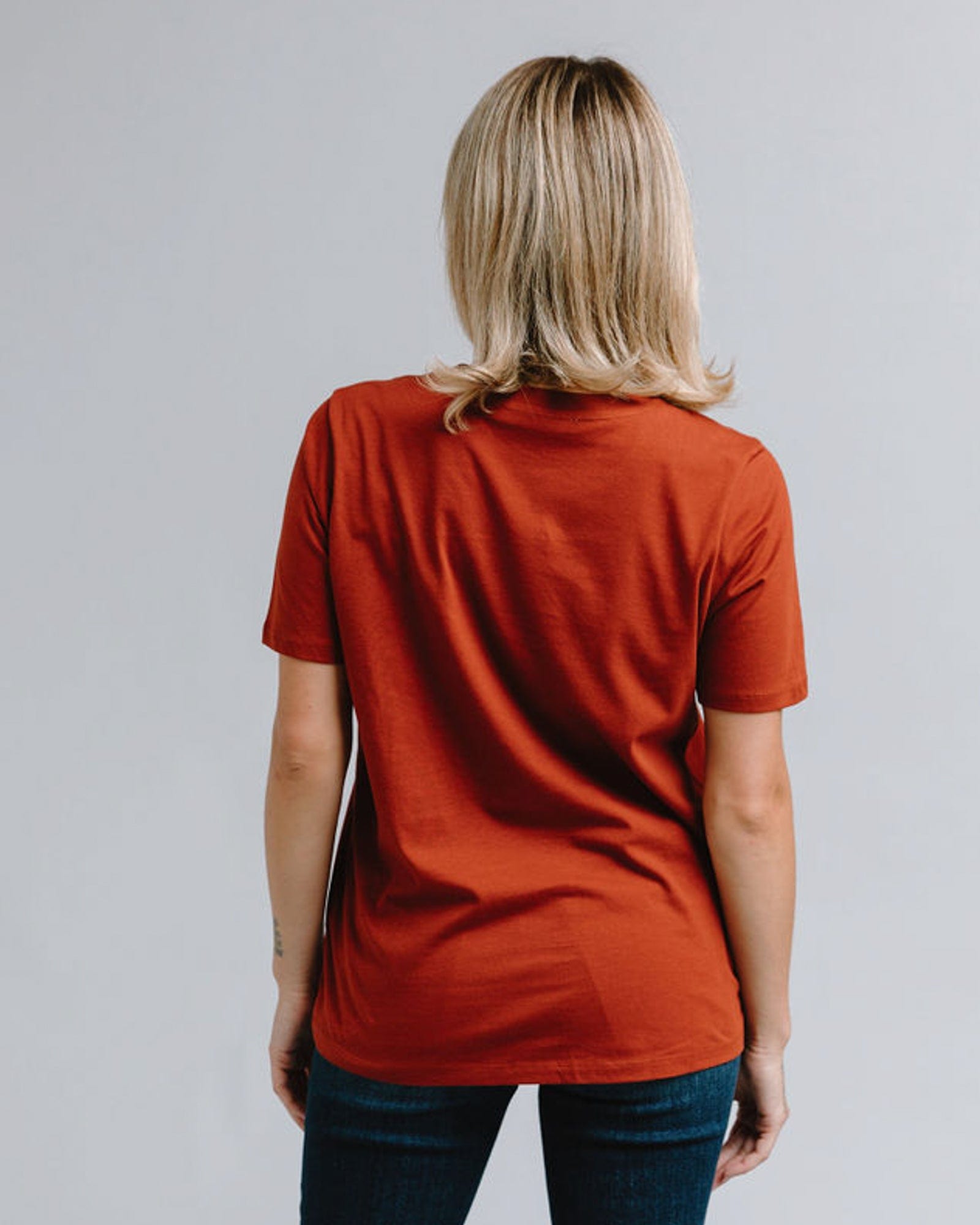 Woman in a short sleeve, burnt orange, graphic tee with embroidered floral on front