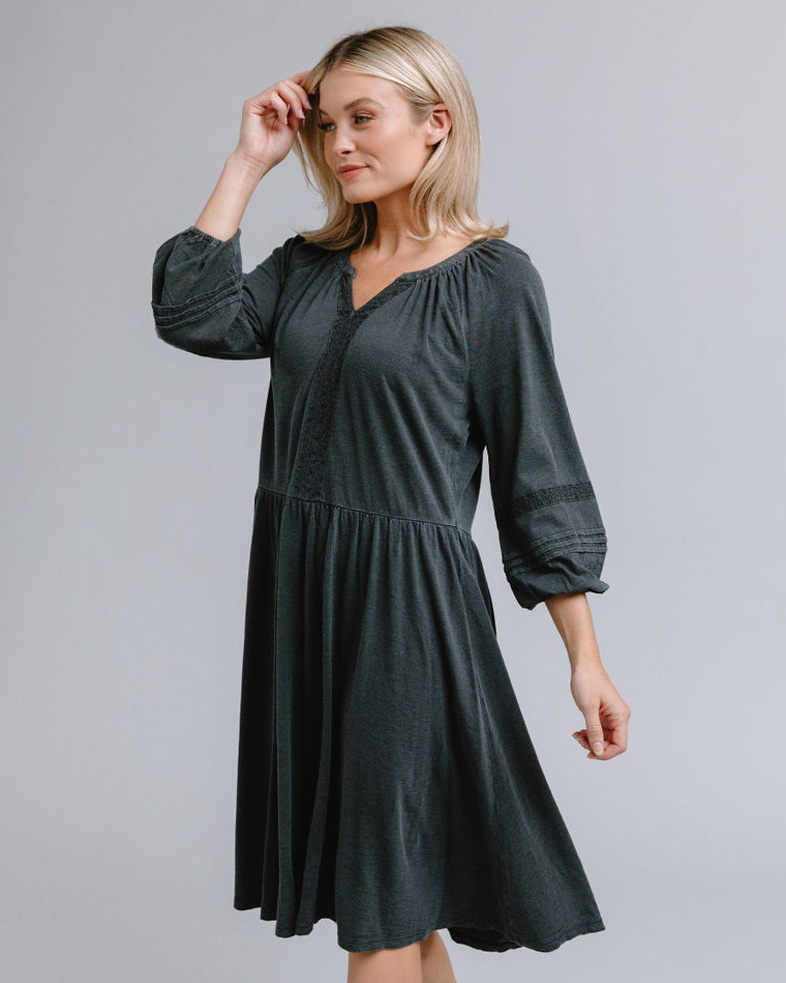 Woman in a 3/4 sleeve, knee-length, gray dress with lace detail around neckline