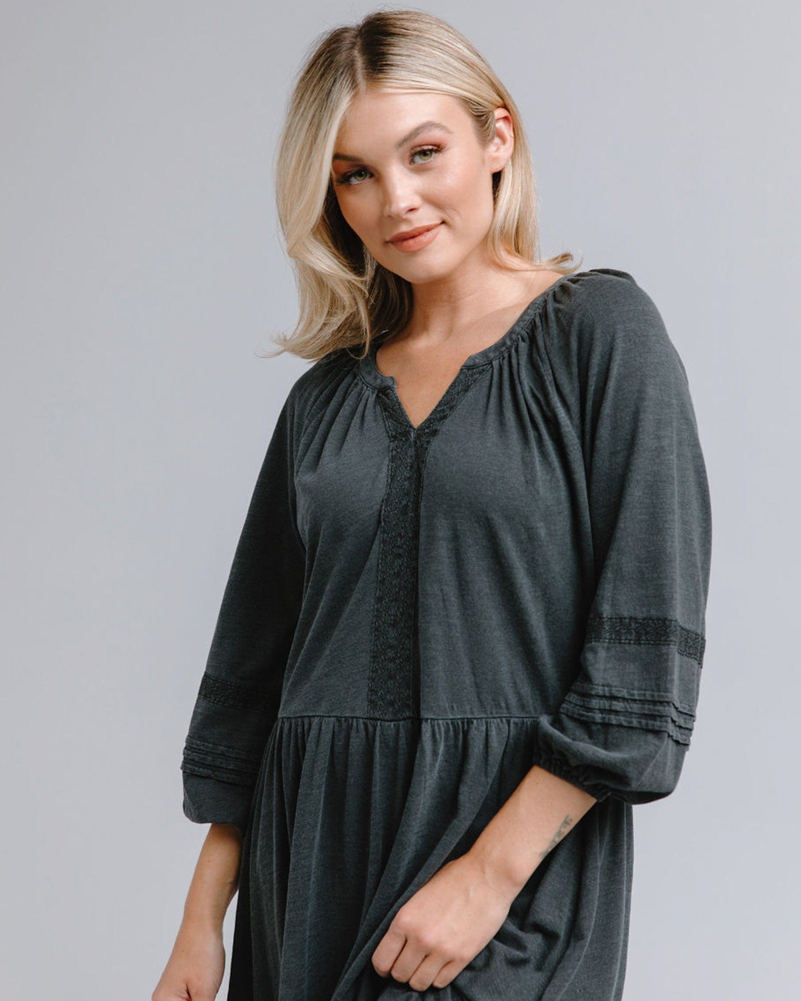 Woman in a 3/4 sleeve, knee-length, gray dress with lace detail around neckline