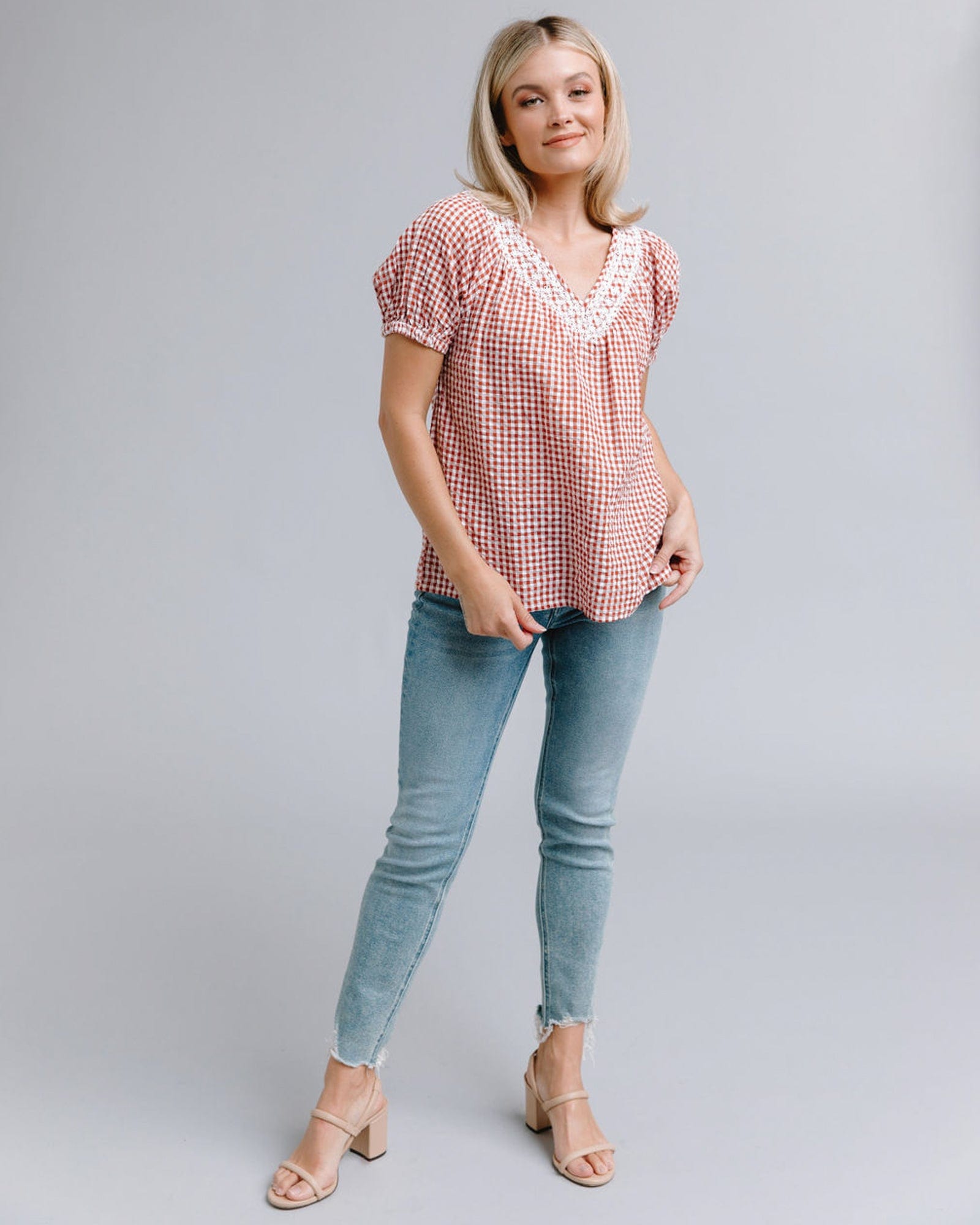 Woman in a red and white plaid, short sleeve, v-neck top with lace along neckline