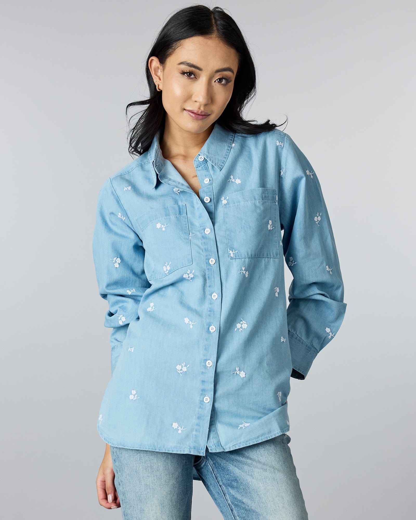 Woman in a long sleeve, chambray button-down top with floral embroidery.