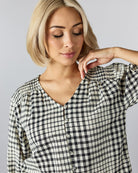 Woman in a 3/4 length v-neck blouse with plaid pattern and buttons down front.