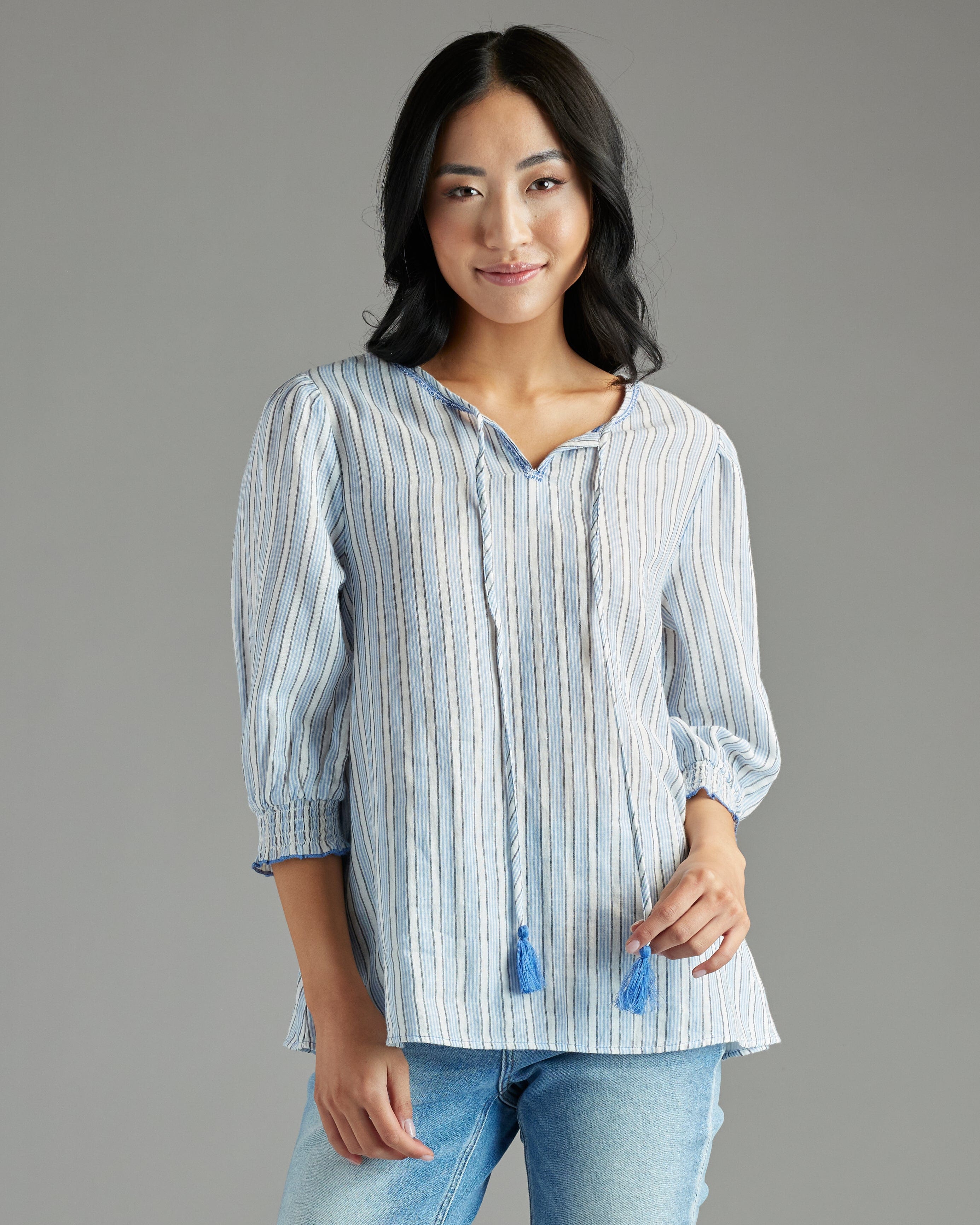 Woman in a blue blouse with 3/4 length sleeves, vertical stripes and tassels