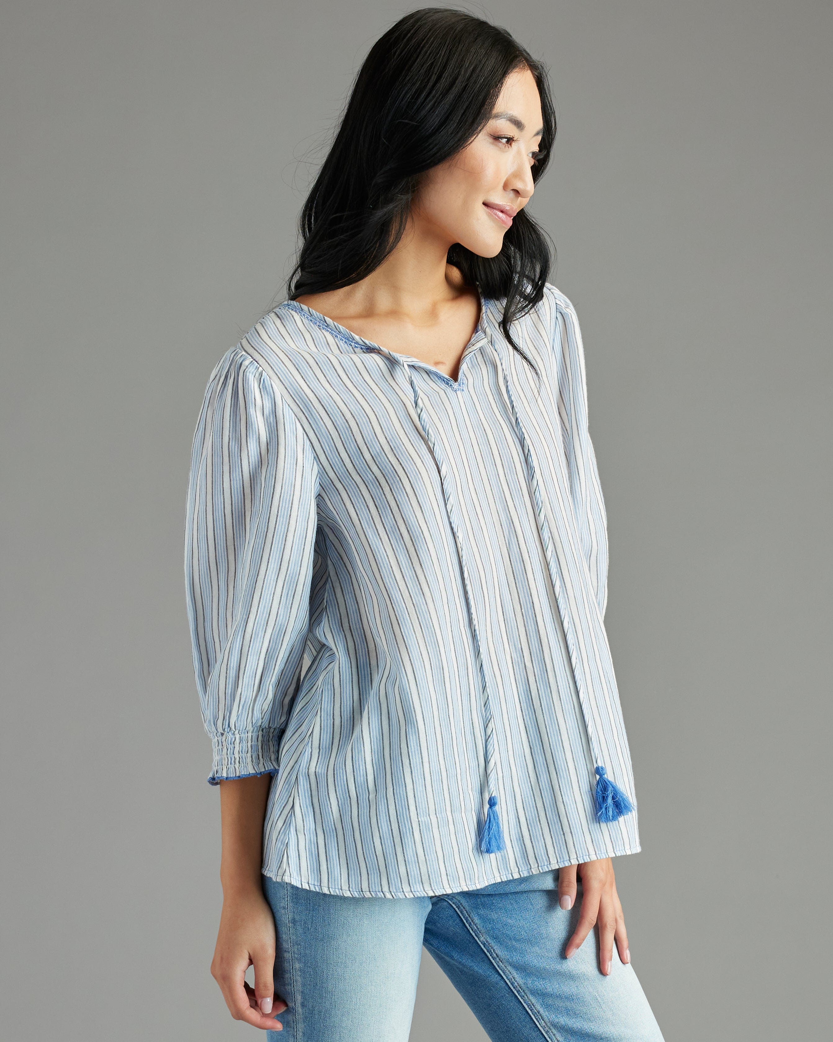 Woman in a blue blouse with 3/4 length sleeves, vertical stripes and tassels