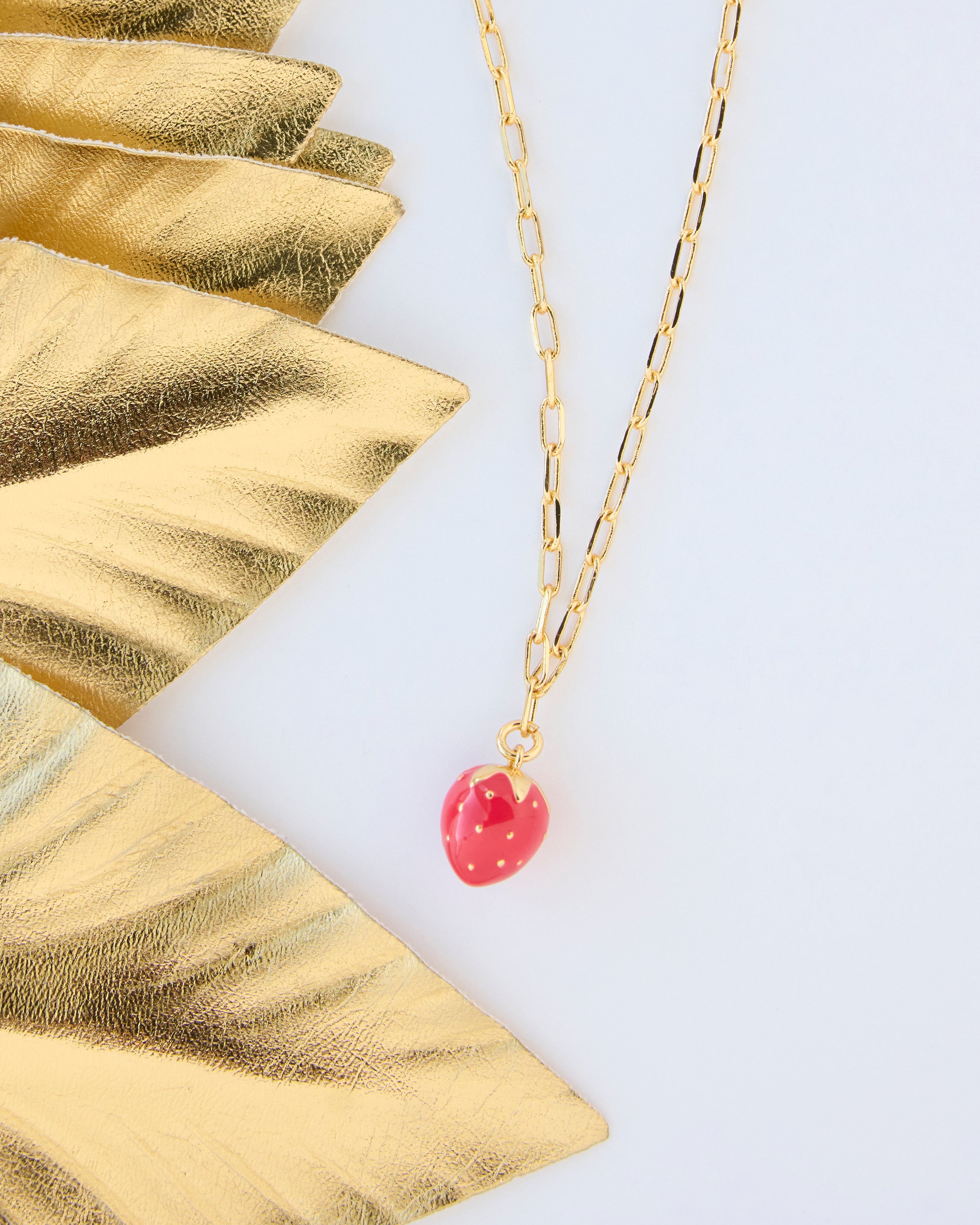 Gold necklace with a red strawberry charm.