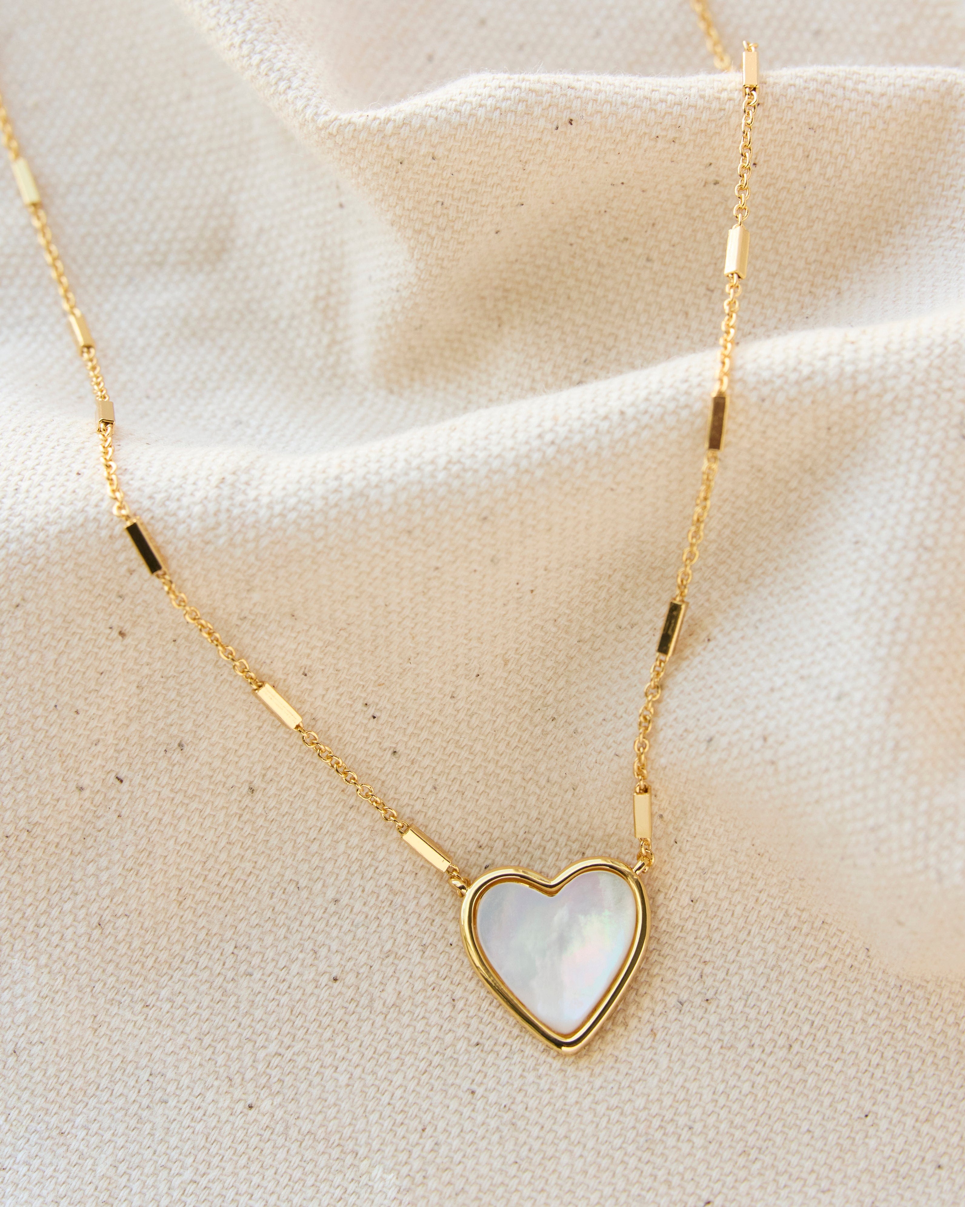 Gold necklace with mother of pearl pendant in heart shape.