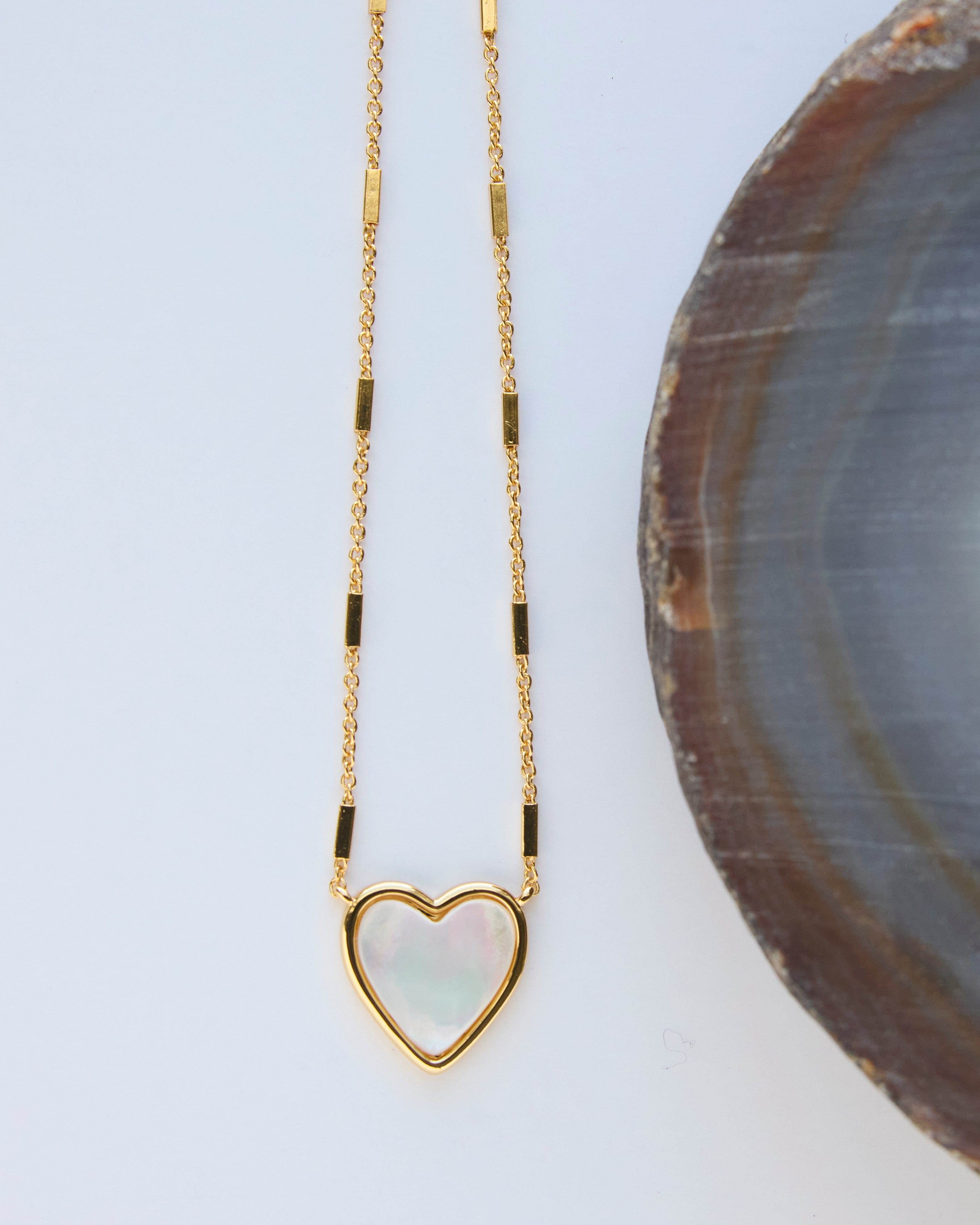 Gold necklace with mother of pearl pendant in heart shape.