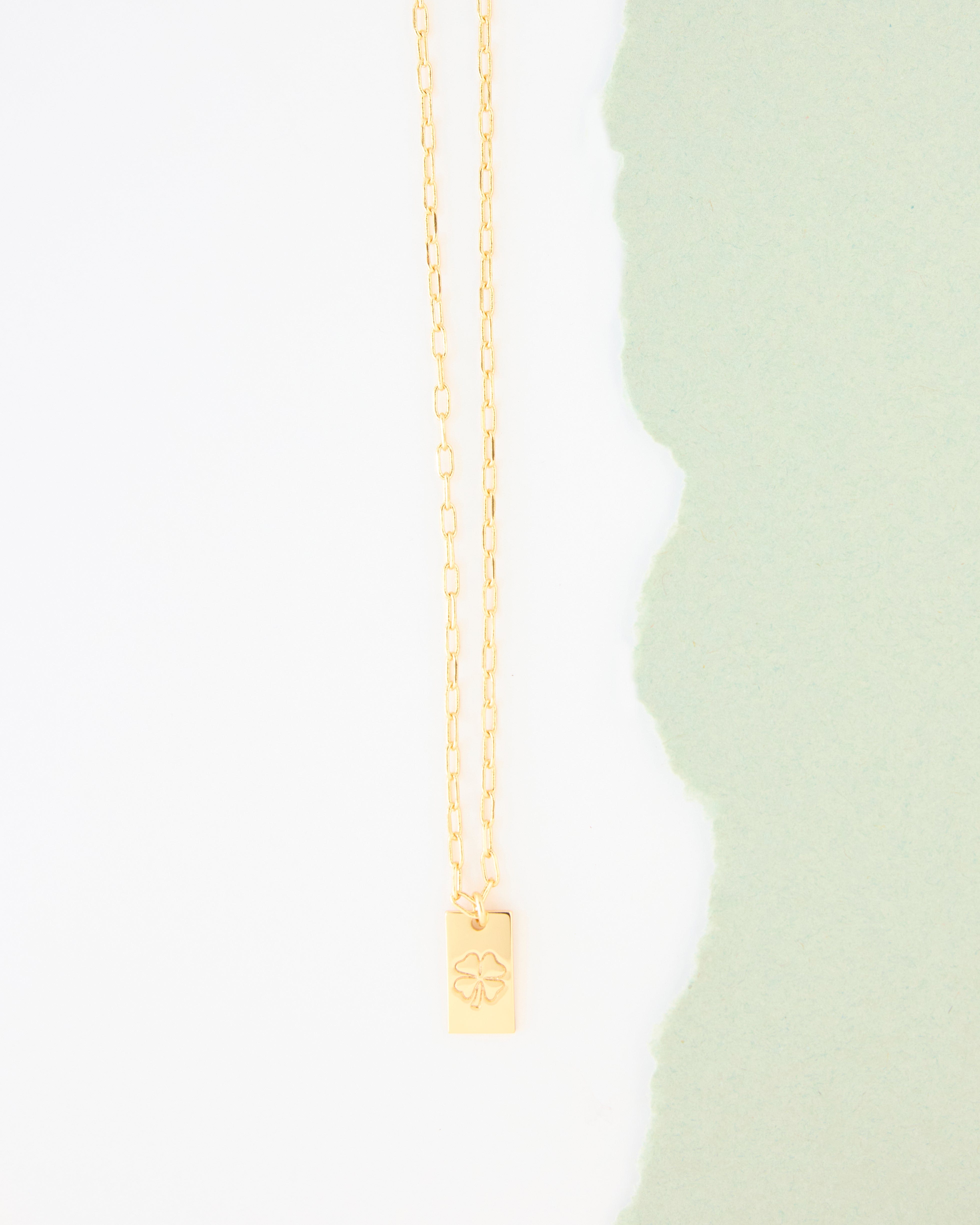 Gold necklace with four leaf clover on charm.