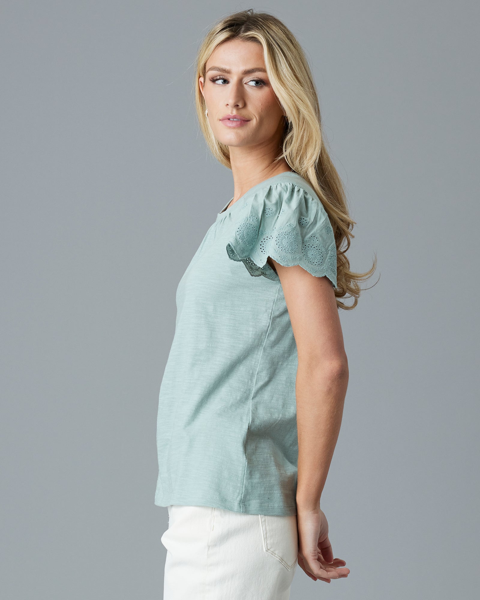 Woman in a green, short sleeved t-shirt with eyelet detail on sleeves.