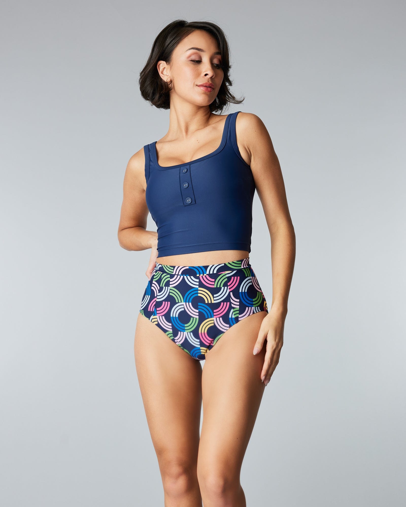Woman in a two-piece swimsuit with a solid blue top and a rainbow print and patterned bottom.
