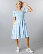 Woman in a blue short sleeved, knee length dress with smocking on bodice.