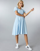 Woman in a blue short sleeved, knee length dress with smocking on bodice.