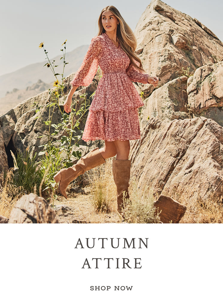 Text over image "Autumn Attire. Shop Now". A women in a pink dress in the middle of a rocky path.