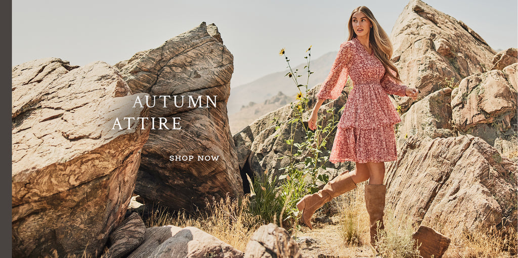 Text over image "Autumn Attire. Shop Now". A women in a pink dress in the middle of a rocky path.