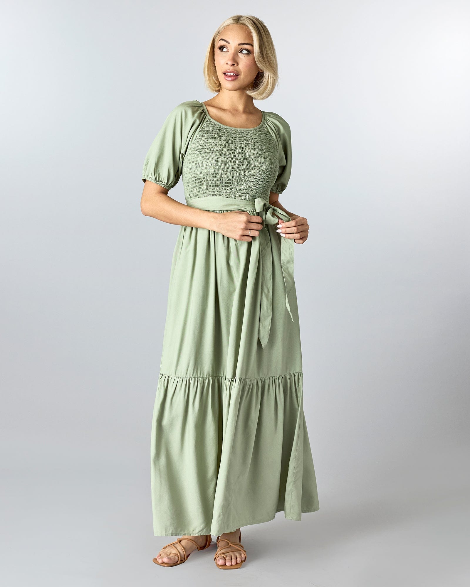 Woman in a green, short sleeved, maxi-length dress with smocking on bodice and a tie at the waist.