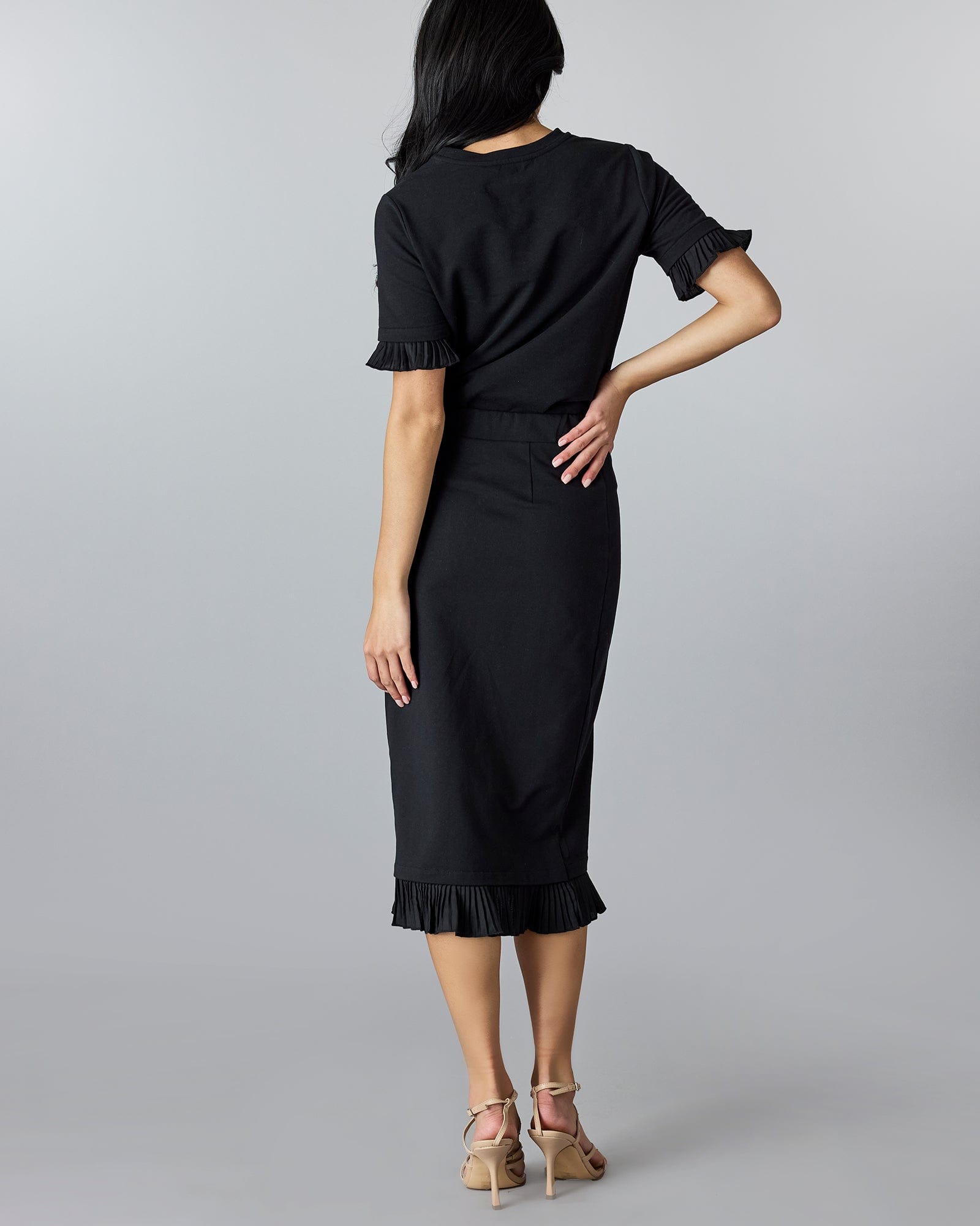 Woman in a black pencil skirt with ruffle at bottom.